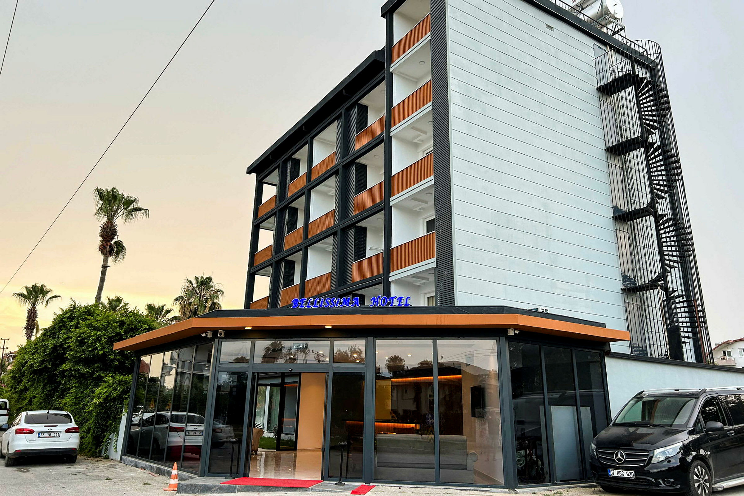 Bygningen er et moderne hotel med fem etager og glasindgang. Skiltet "Bellissima Hotel" vises på indgangen. (AI-genereret tekst)