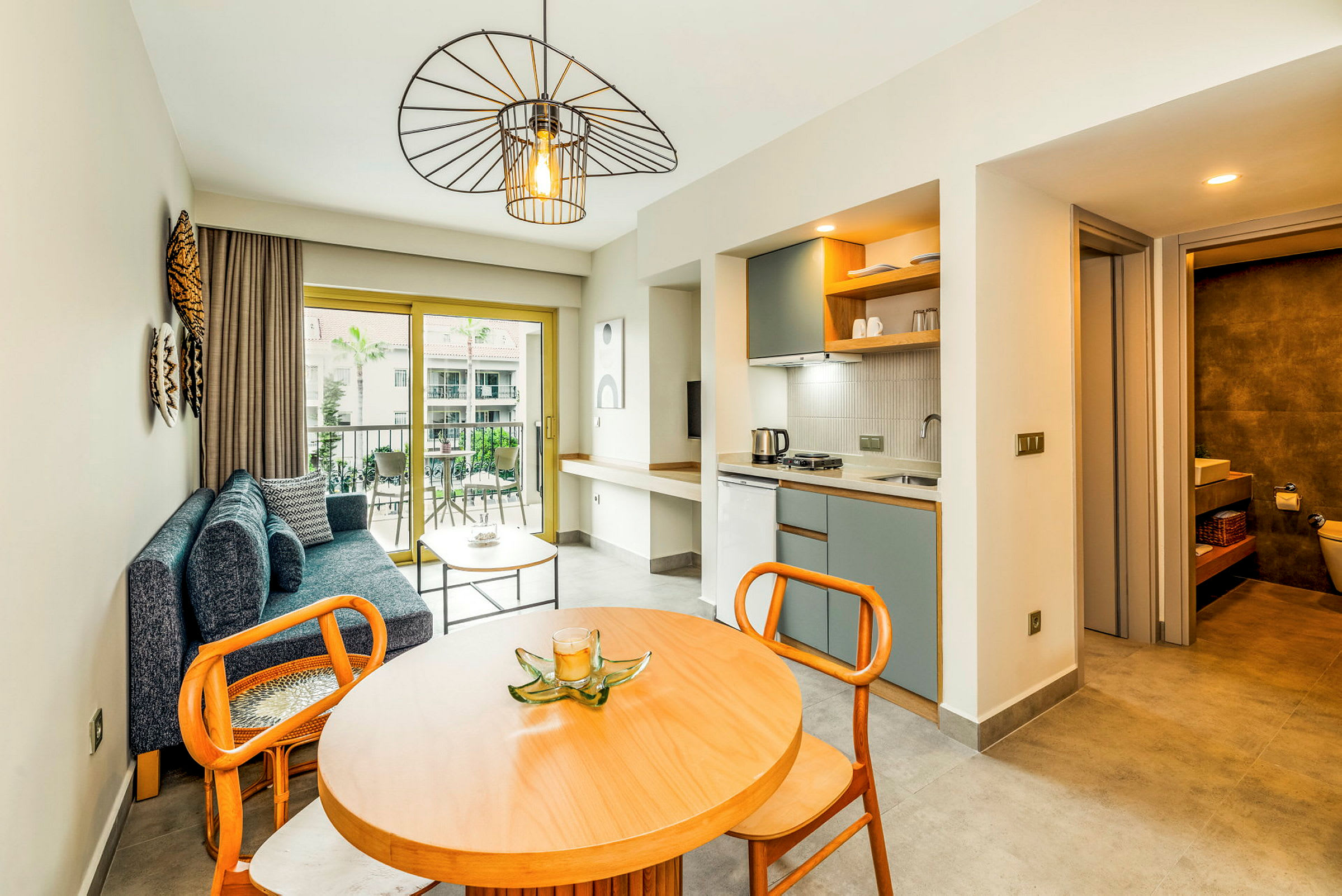 Et moderne hotelværelse med siddeområde, spisebord, køkkenområde og et badeværelse i baggrunden. (AI-genereret tekst)