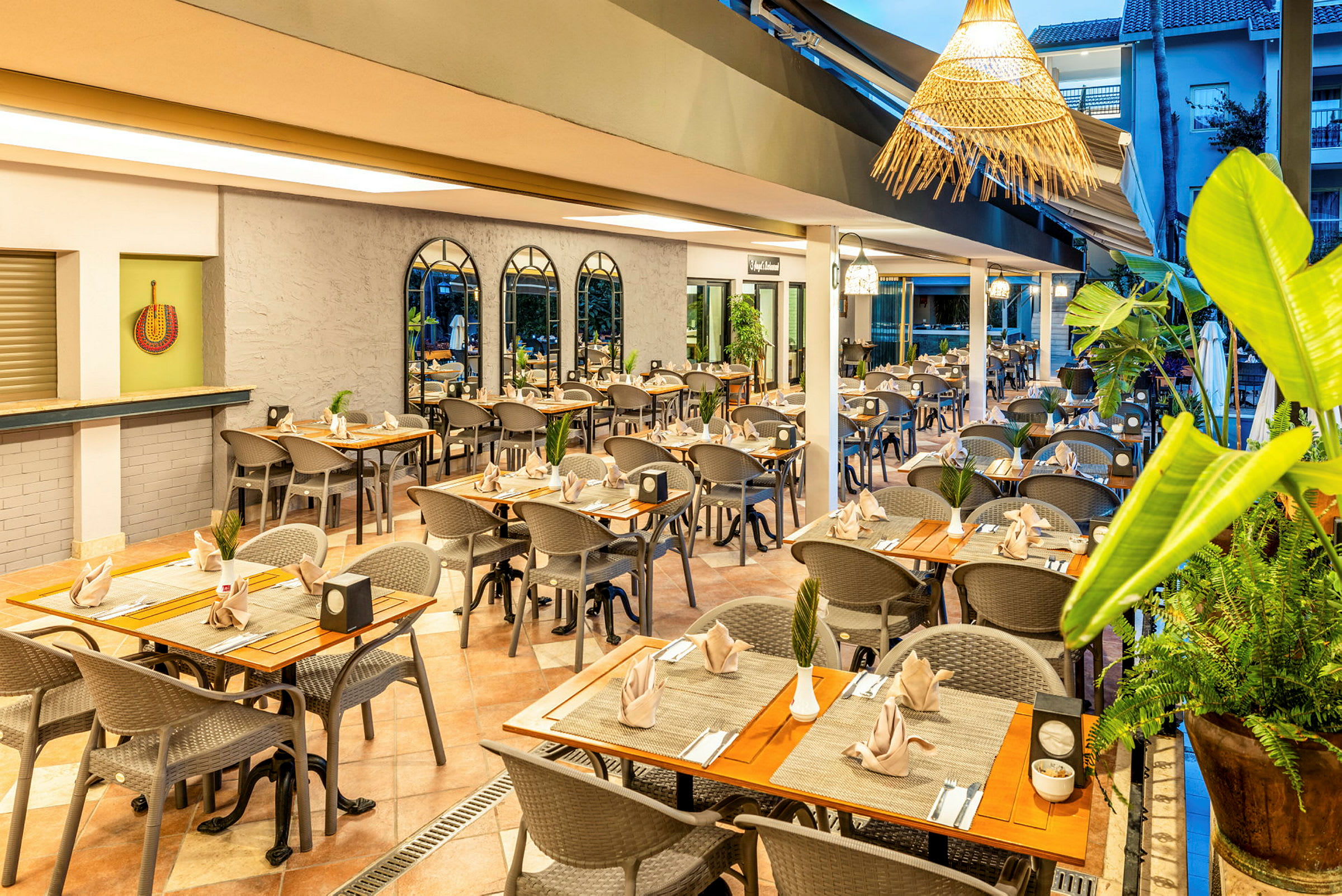 En restaurantmiljø med oprettede borde og stole, dekoreret med planter og velplacerede servietter. (AI-genereret tekst)