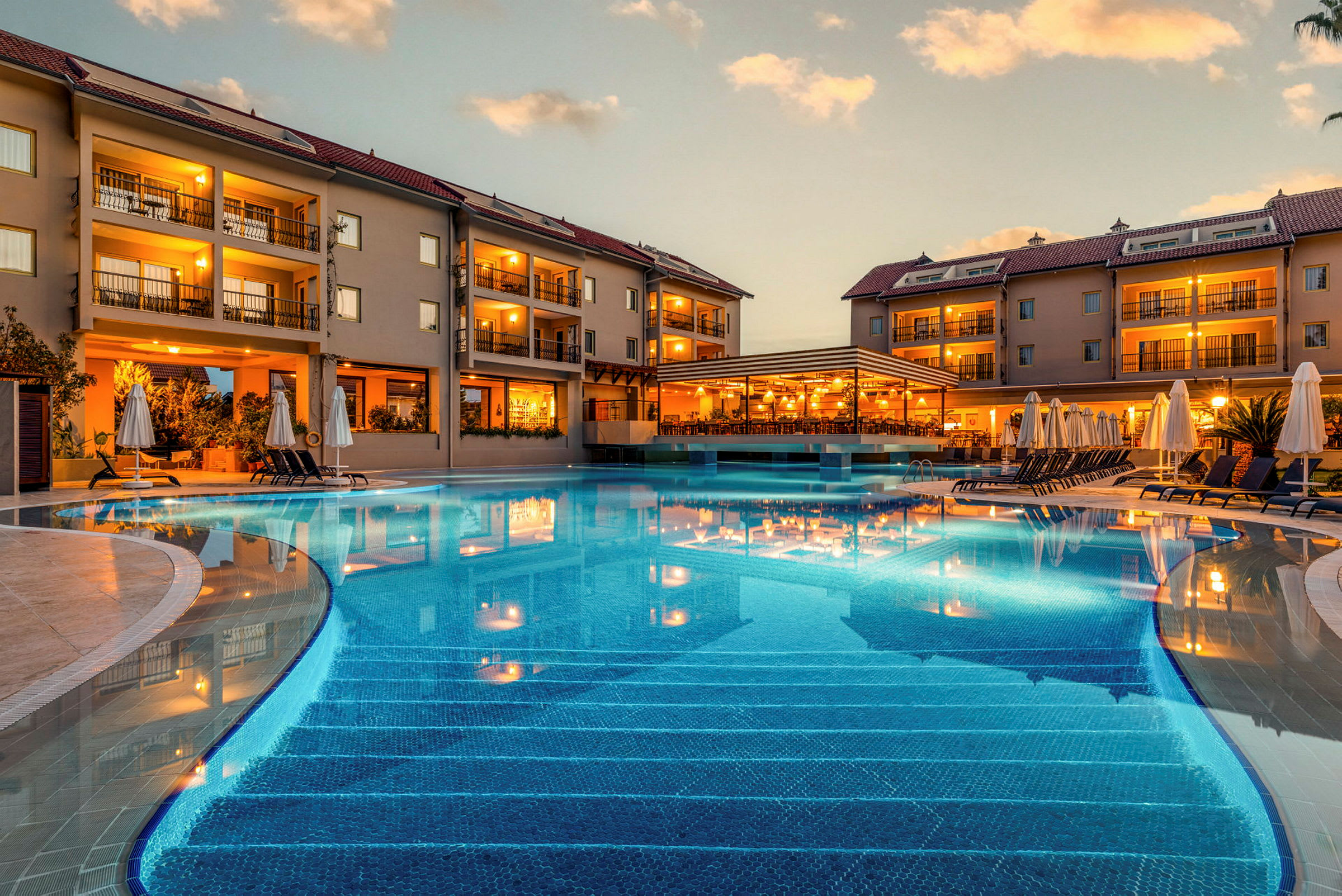 Hotelkompleks med pool og liggestole ved skumring. (AI-genereret tekst)
