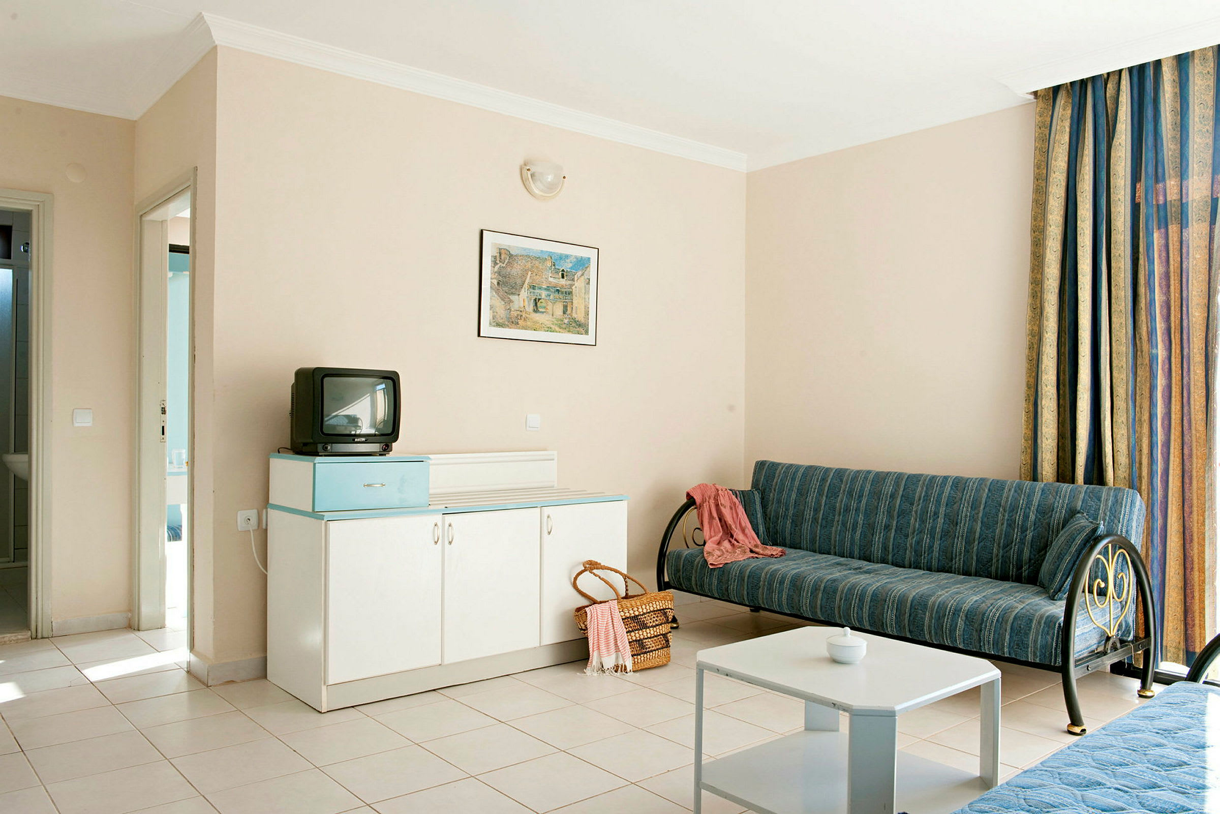 Hotelværelse med sofa, bord, skab og lille tv. (AI-genereret tekst)