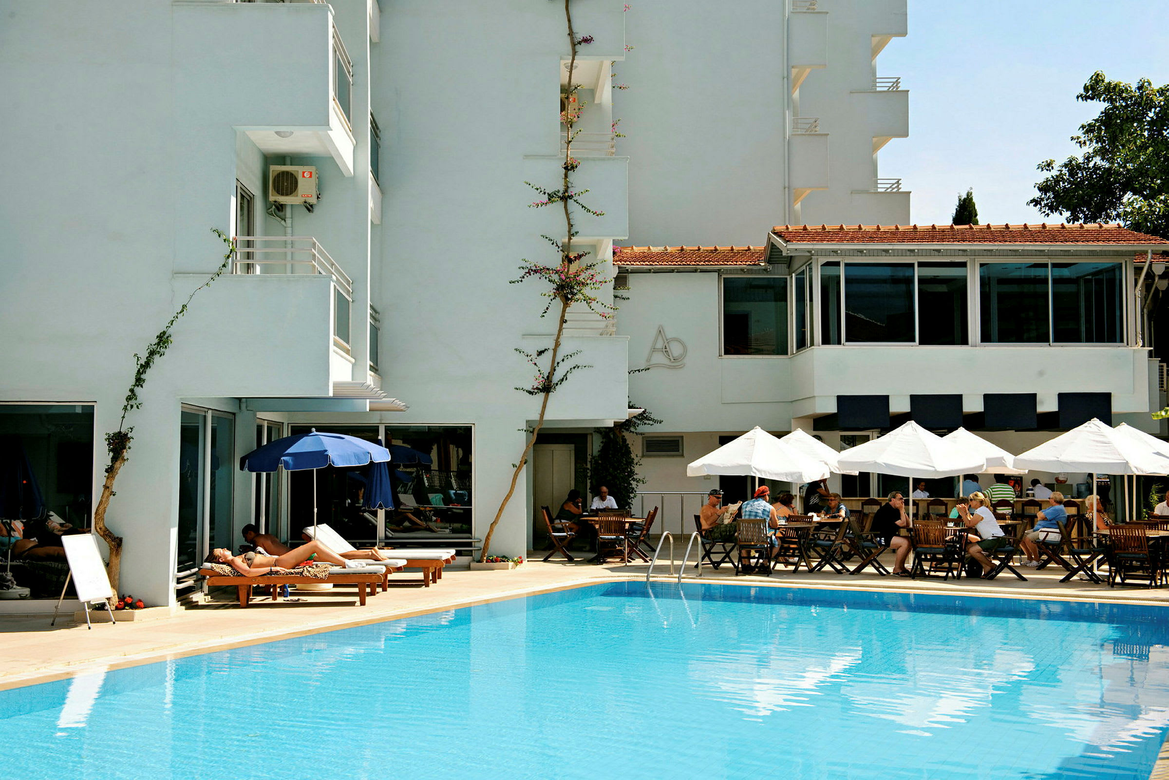 En pool foran et hotel med liggestole og borde under parasoller. (AI-genereret tekst)