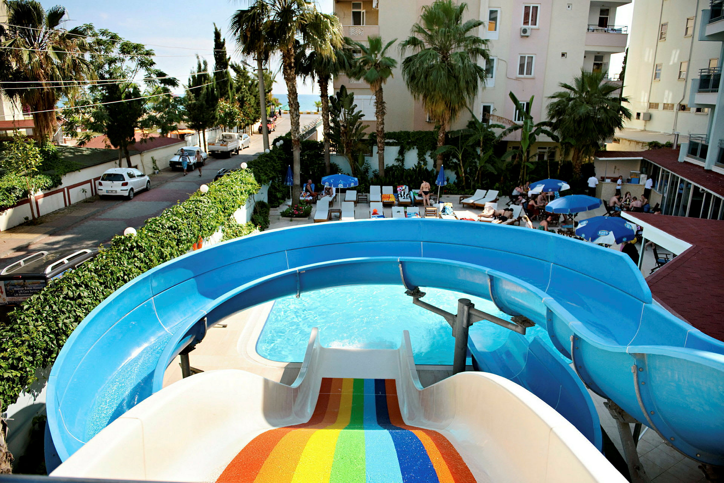 En pool med vandrutsjebane og solsenge i en hotelhave. (AI-genereret tekst)