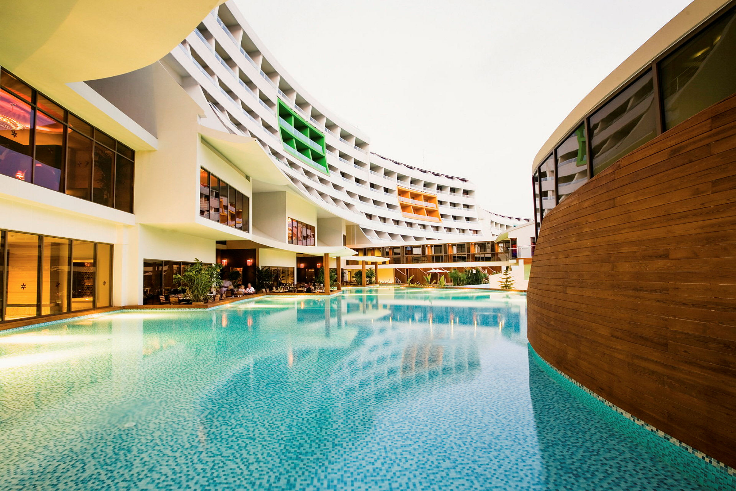 En stor udendørs pool foran et moderne hotel med farverige altaner. (AI-genereret tekst)