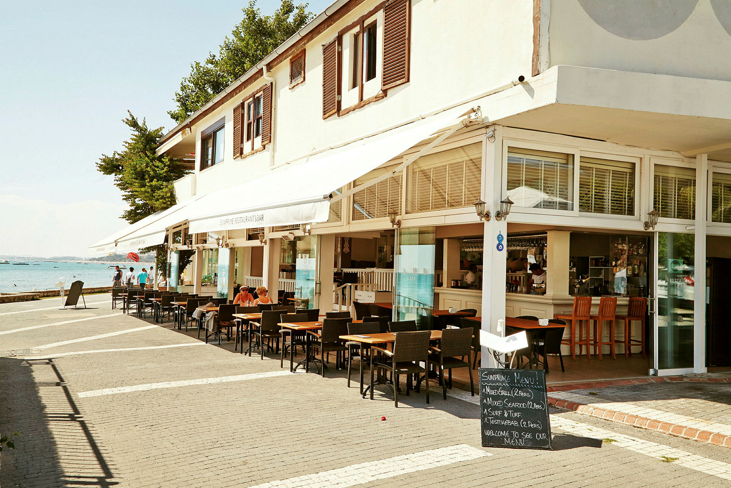 En café eller restaurant med udendørs siddepladser og udsigt til havet. (AI-genereret tekst)