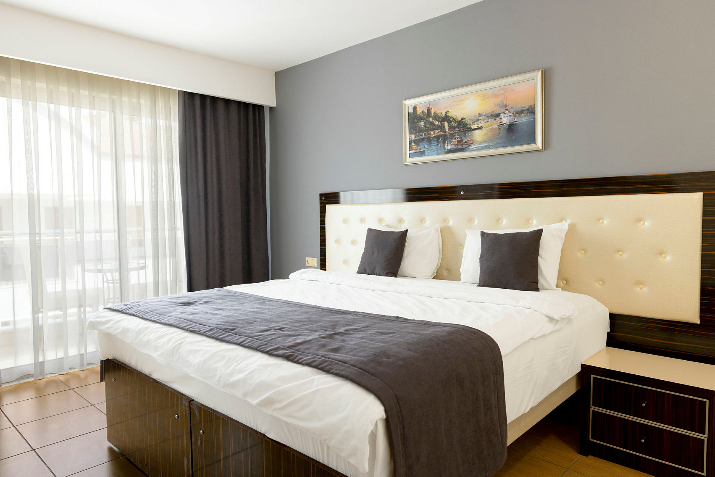 Et moderne hotelværelse med en dobbeltseng, en grå sengeklæde og et maleri på væggen. (AI-genereret tekst)
