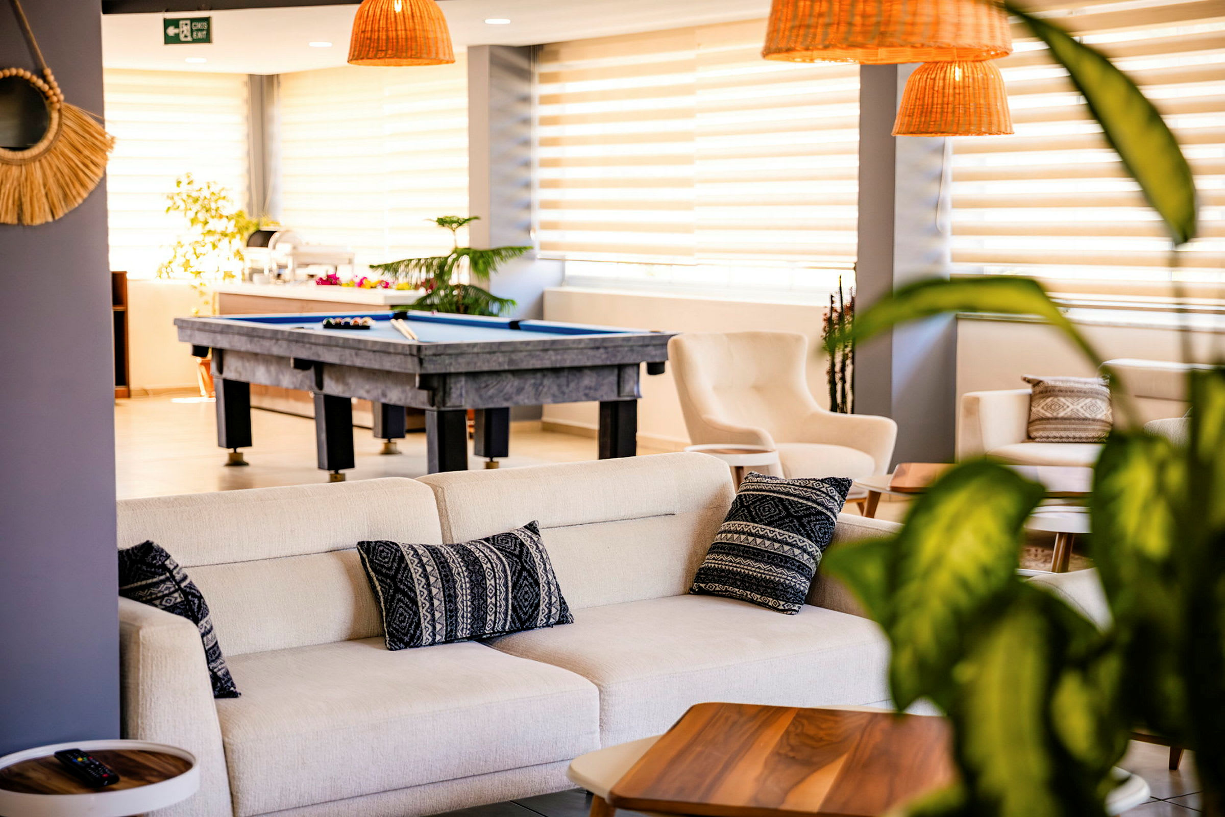 En lys og moderne lounge med sofaer, puder og et poolbord i baggrunden. (AI-genereret tekst)