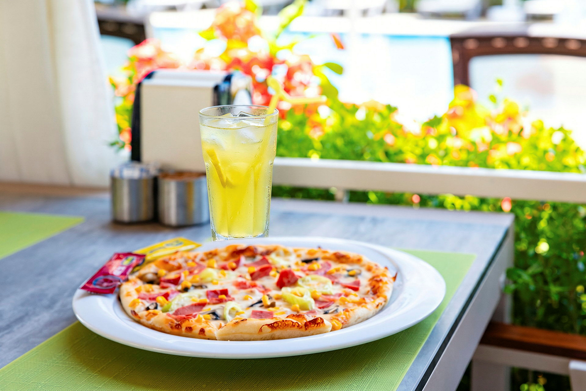 En tallerken med pizza og et glas med gul drik står på et bord udendørs. (AI-genereret tekst)