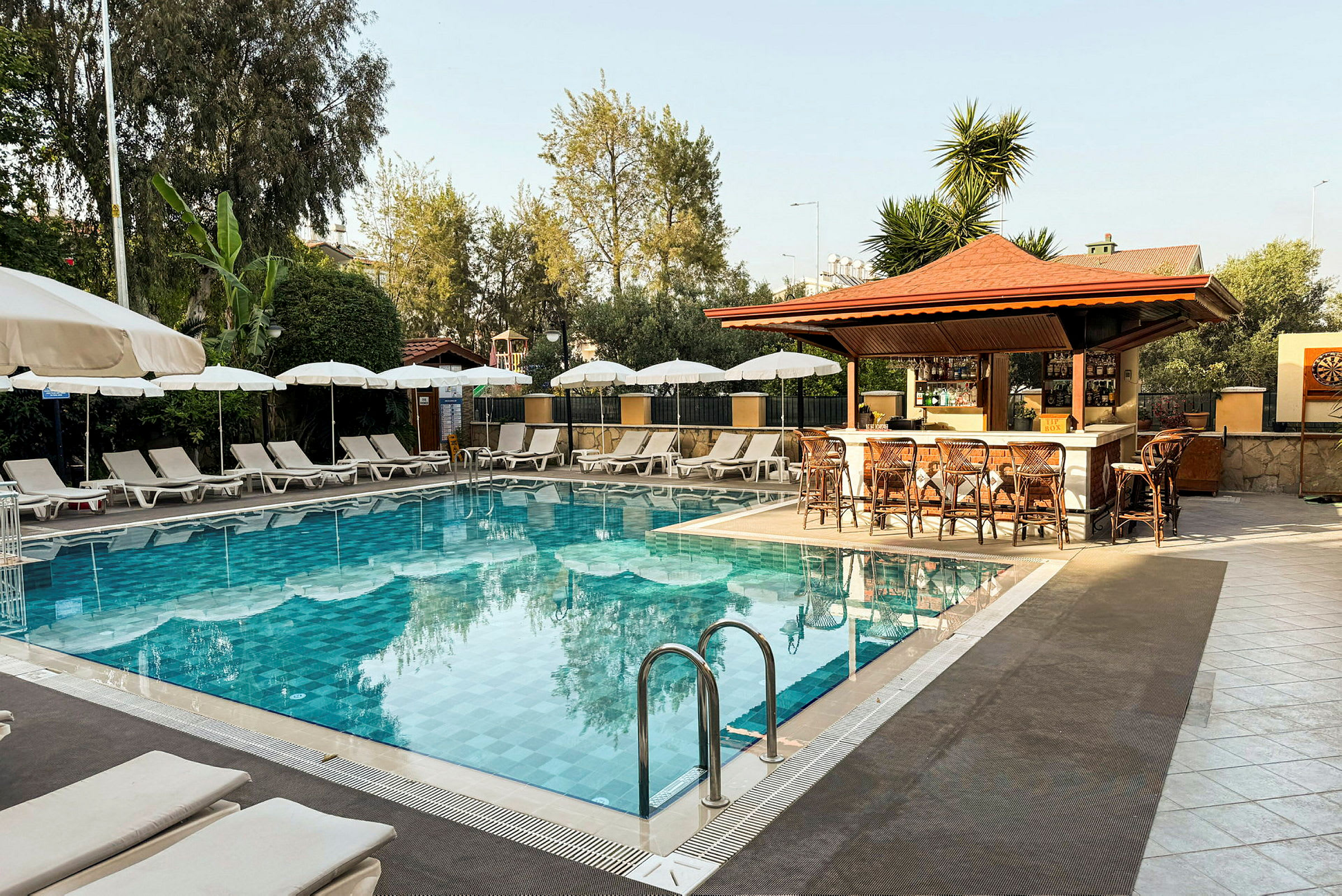 Udendørs swimmingpool med liggestole og parasoller i baggrunden og en bar ved siden af. (AI-genereret tekst)