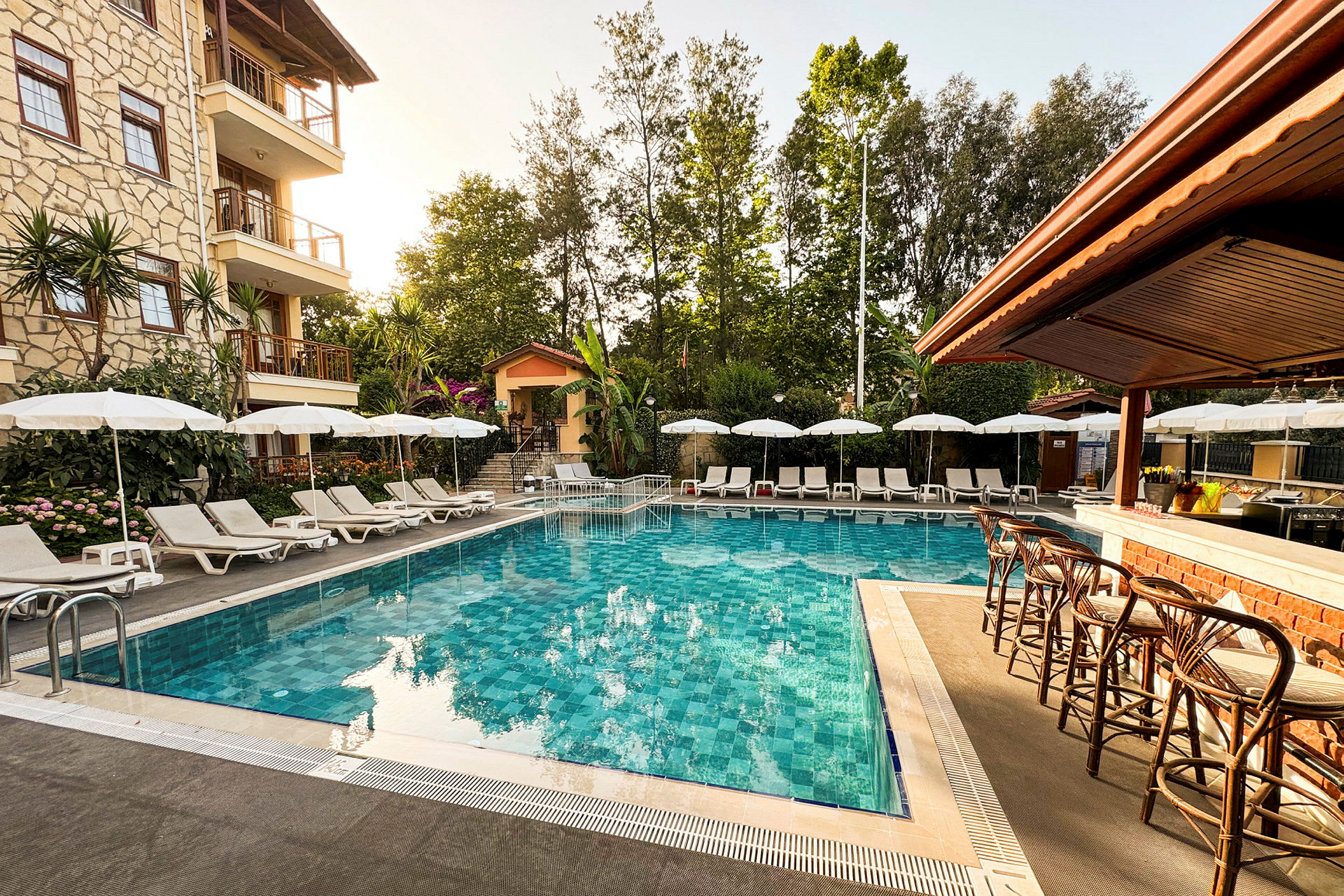 Billede af en udendørs pool omgivet af liggestole, parasoller og en bar. (AI-genereret tekst)