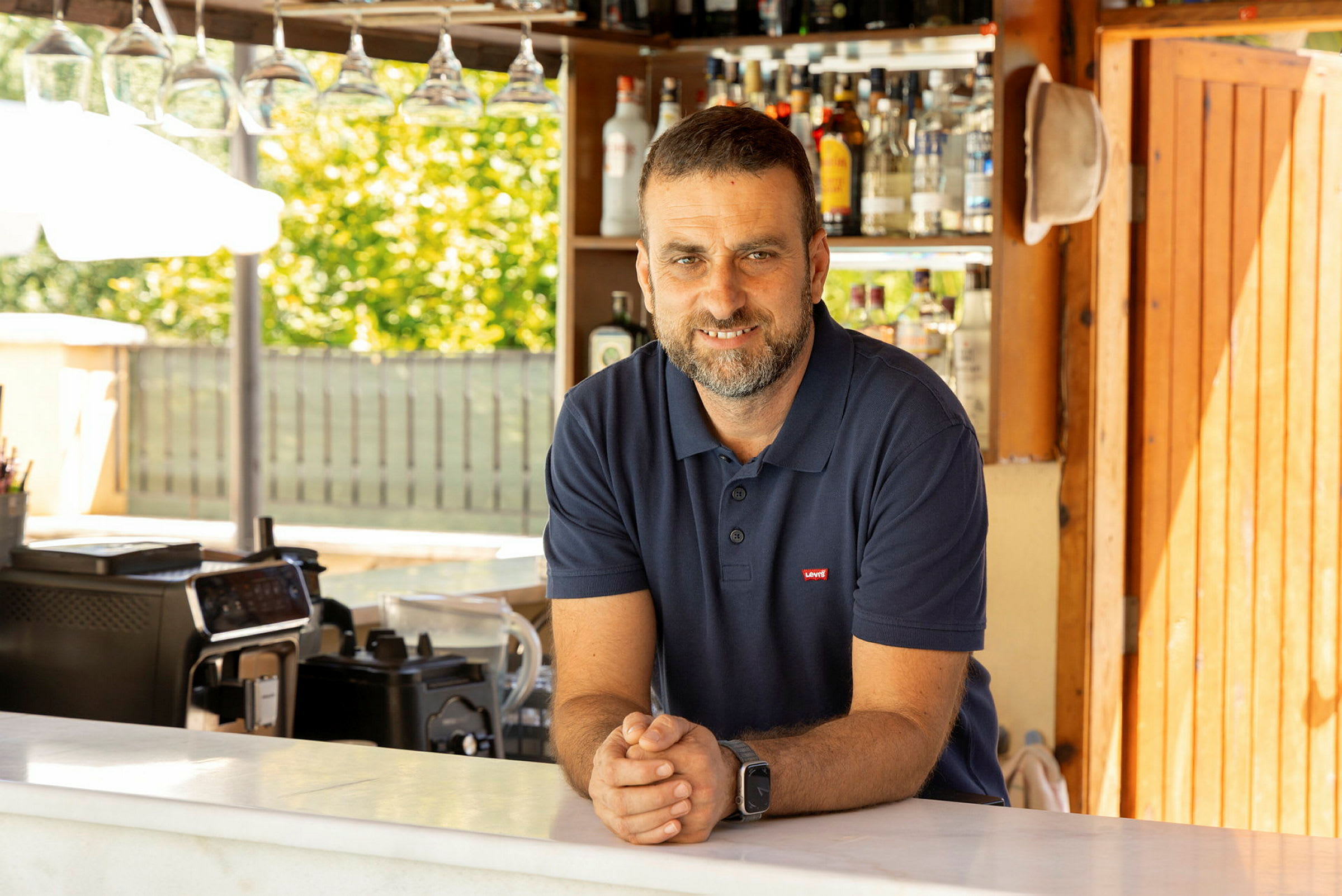 En mand står bag en bar med flasker i baggrunden. (AI-genereret tekst)