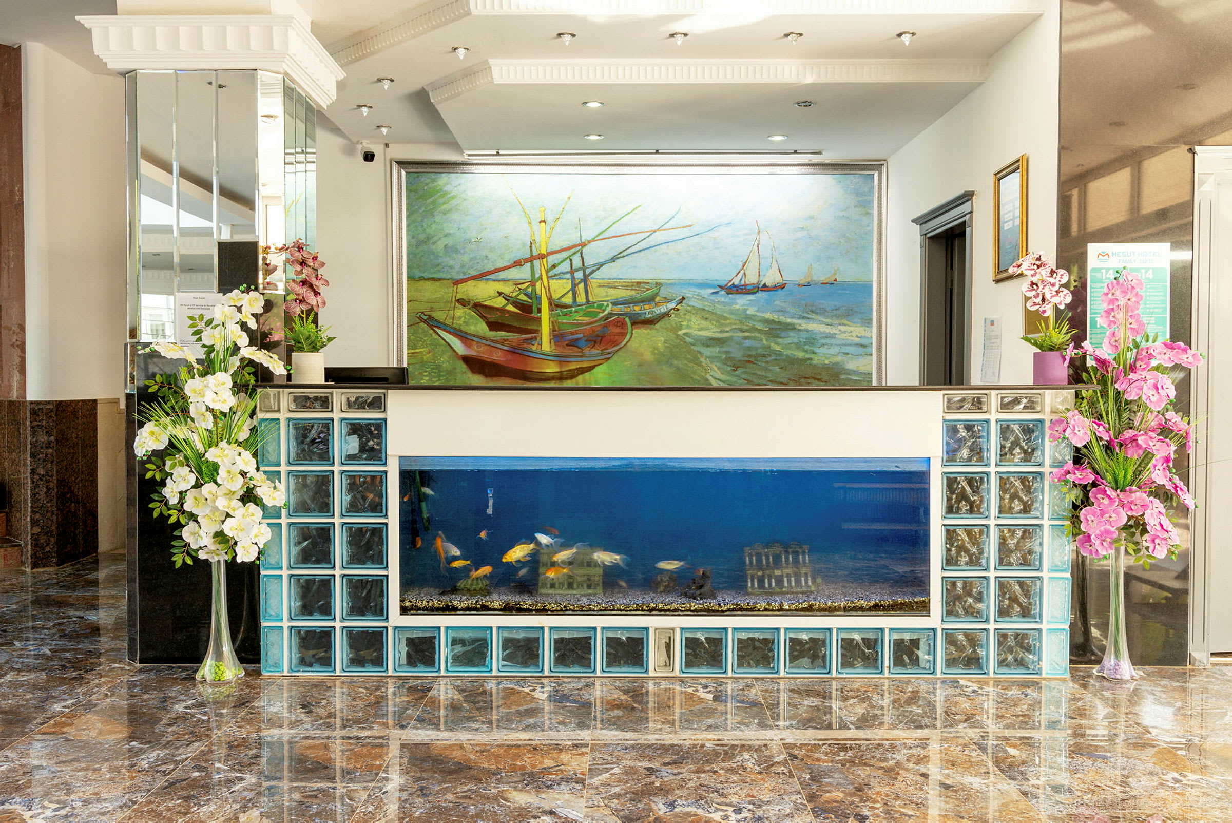 Hotellets lobby med receptionen lavet af glasblokke og akvarium, samt et stort maleri af både på en strand. (AI-genereret tekst)