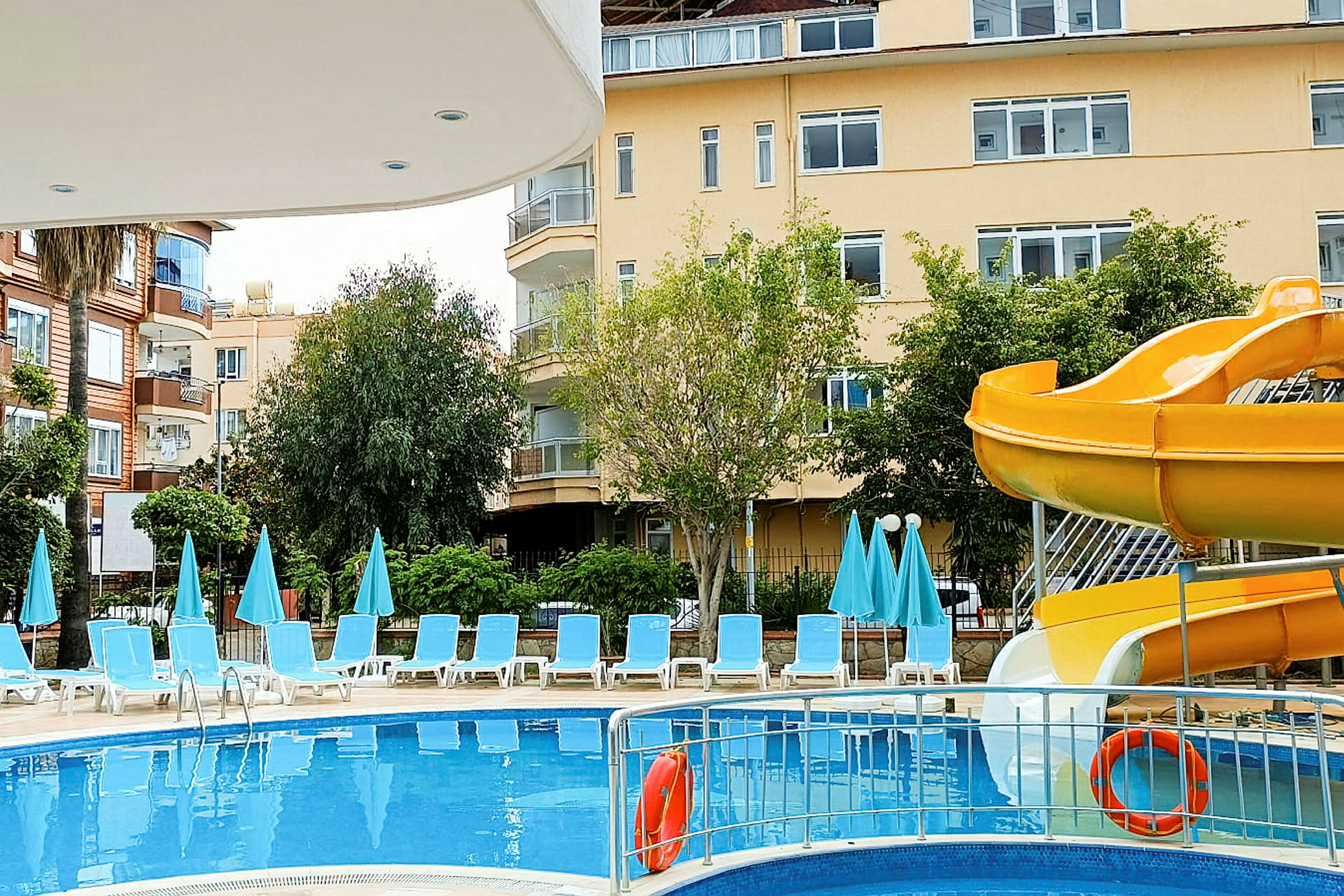 Poolområde med liggestole, parasoller og en gul vandrutsjebane. (AI-genereret tekst)