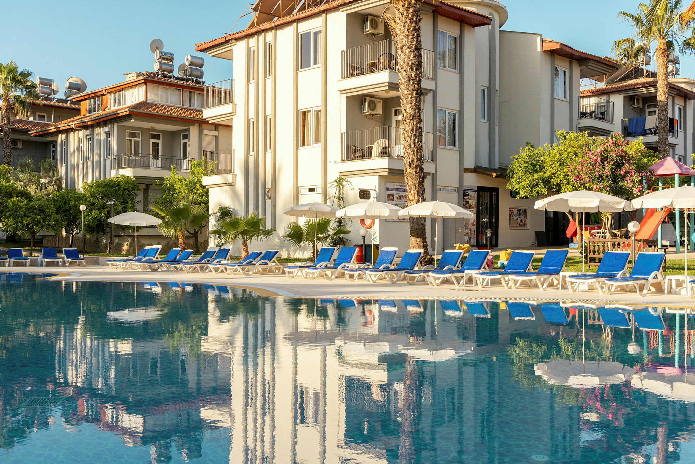 En udendørs pool foran et hotel med liggestole og parasoller. (AI-genereret tekst)
