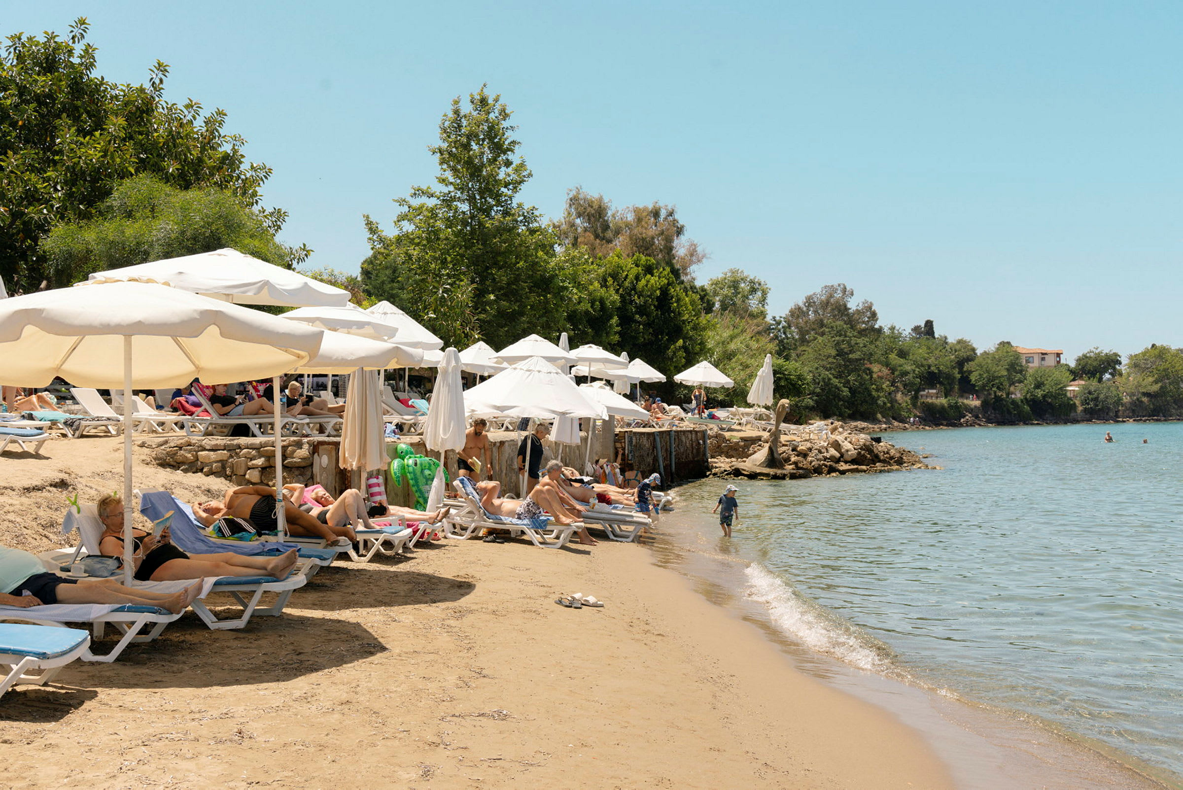 Badestrand med liggestole og parasoller ved kanten af klart vand. (AI-genereret tekst)
