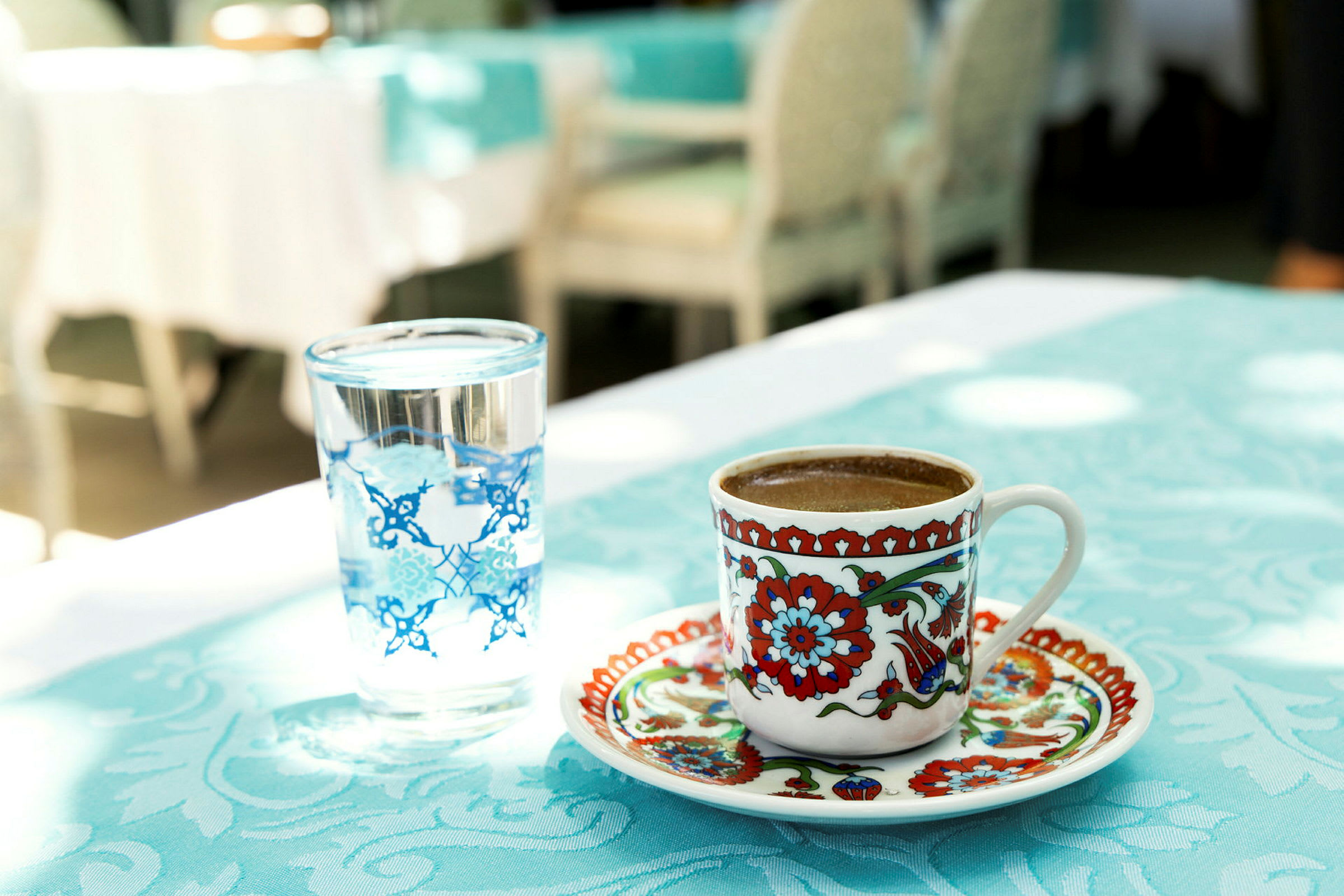 En kop med farverigt mønster indeholdende kaffe ved siden af et glas vand på et bord. (AI-genereret tekst)