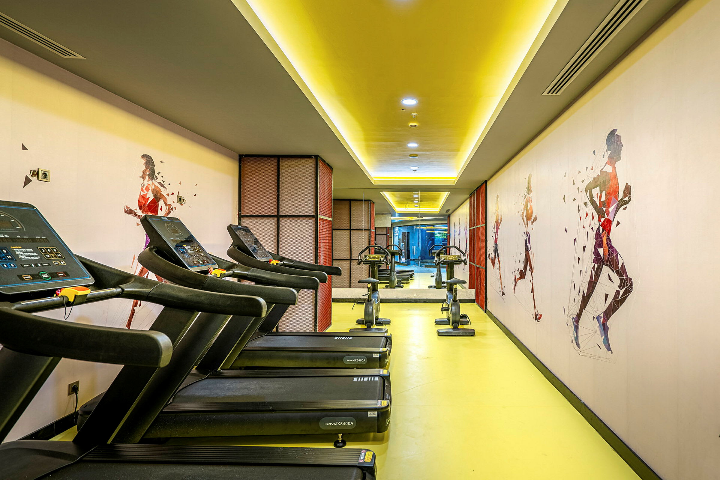 Fitnesscenter med løbebånd og motionscykler, samt vægge dekoreret med løbende silhuetter. (AI-genereret tekst)