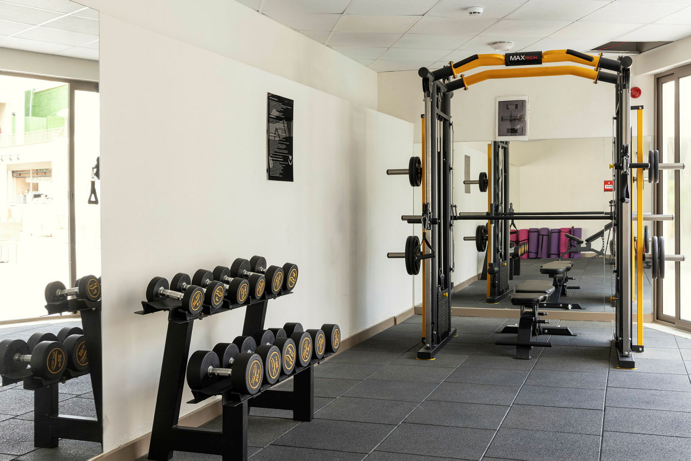 Billede af et fitnesscenter med et vægtstangsstativ og en hylde med håndvægte ved siden af. (AI-genereret tekst)