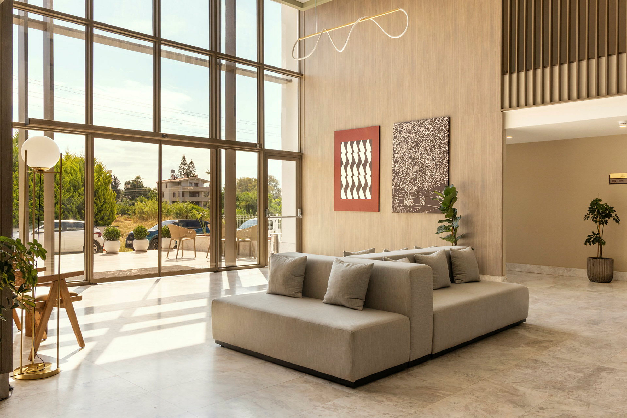 Et moderne hotellobbyområde med store glasvinduer, der lader masser af lys ind, dekorative planter og en komfortabel siddegruppe. (AI-genereret tekst)