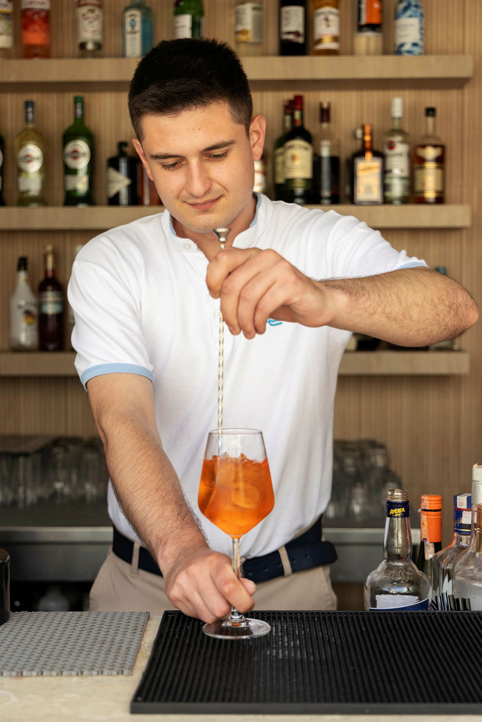 En bartender blander en drink med orange væske i et vinglas. (AI-genereret tekst)