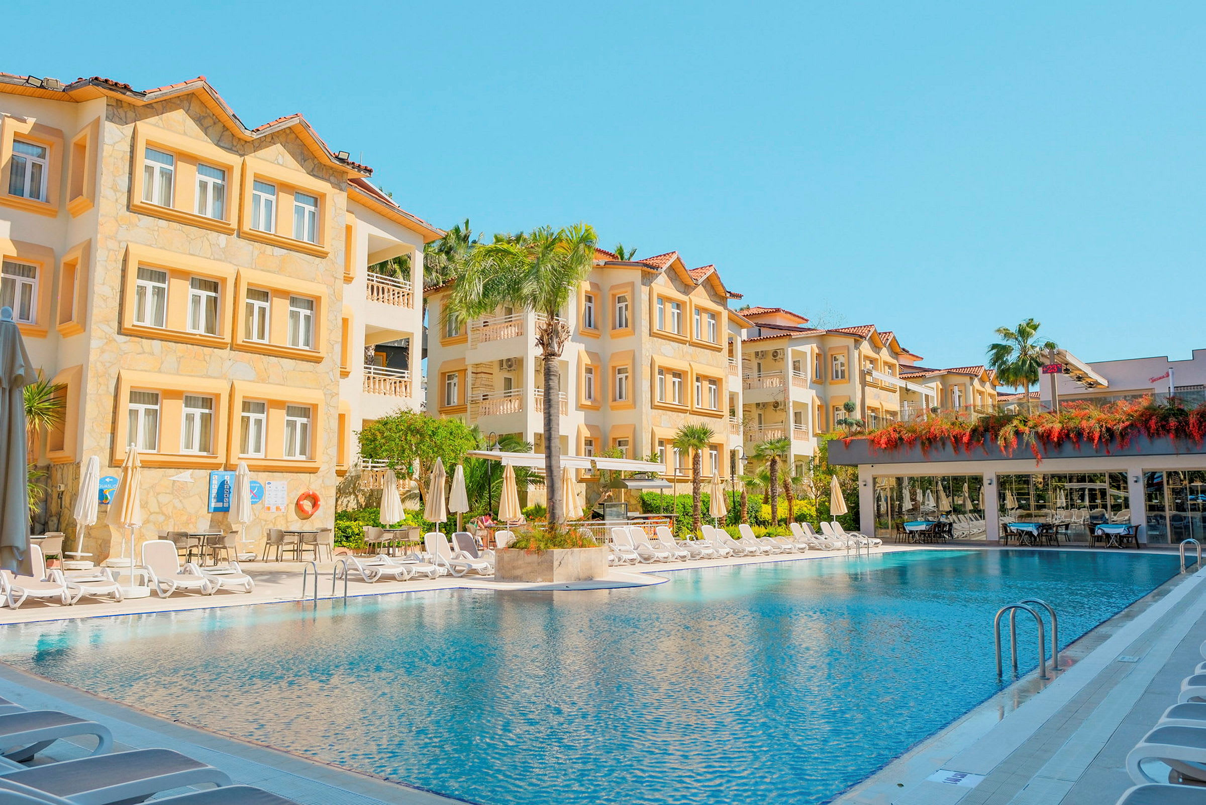 Hotellets facade og udendørs pool under klar blå himmel. (AI-genereret tekst)