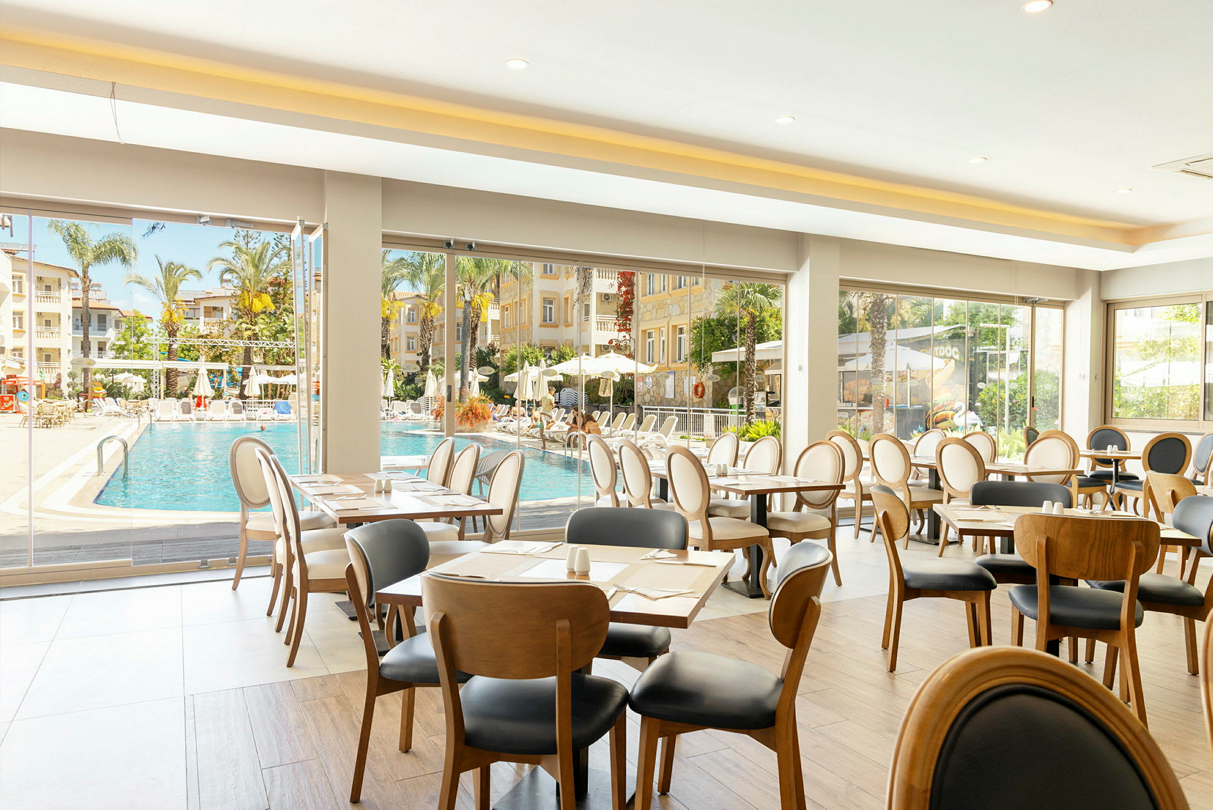 Interiør af restaurant med udsigt til poolområde og palmer. (AI-genereret tekst)