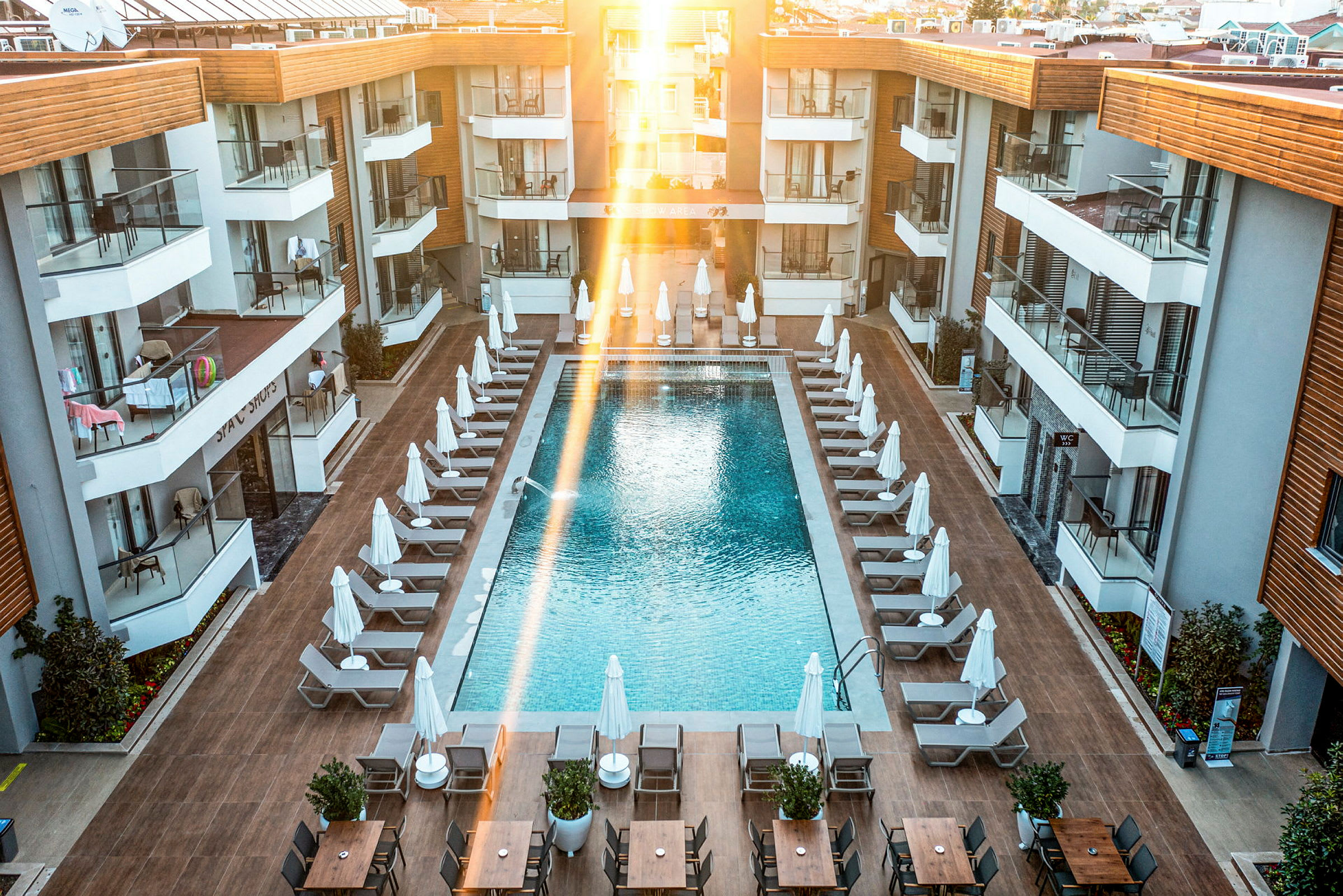 Billede af et hotelpoolområde med liggestole og parasoller omkring en rektangulær pool, omgivet af moderne hotelbygninger. (AI-genereret tekst)
