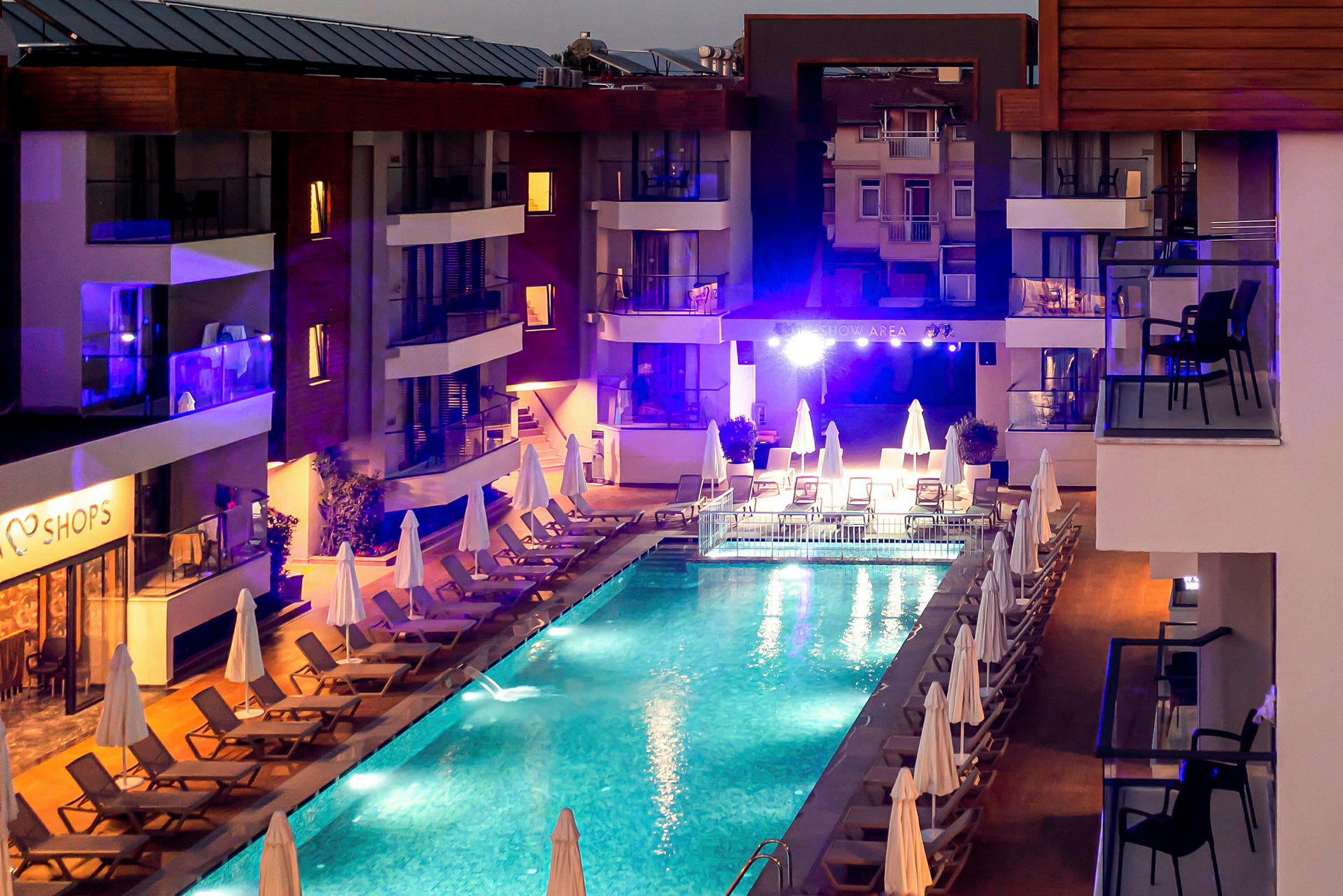 Udsigt over en oplyst pool om aftenen, omgivet af liggestole og parasoller ved et hotel. (AI-genereret tekst)