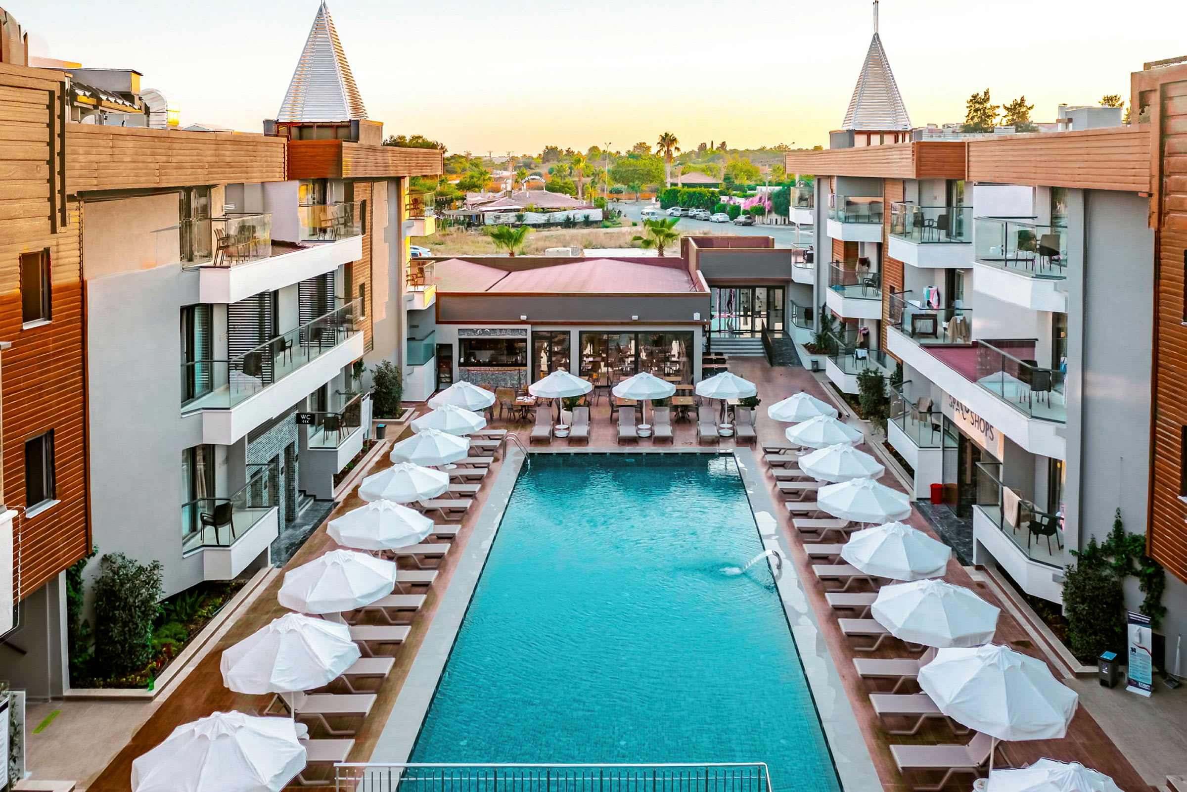 Lejlighedshotel med pool omgivet af liggestole og parasoller. (AI-genereret tekst)