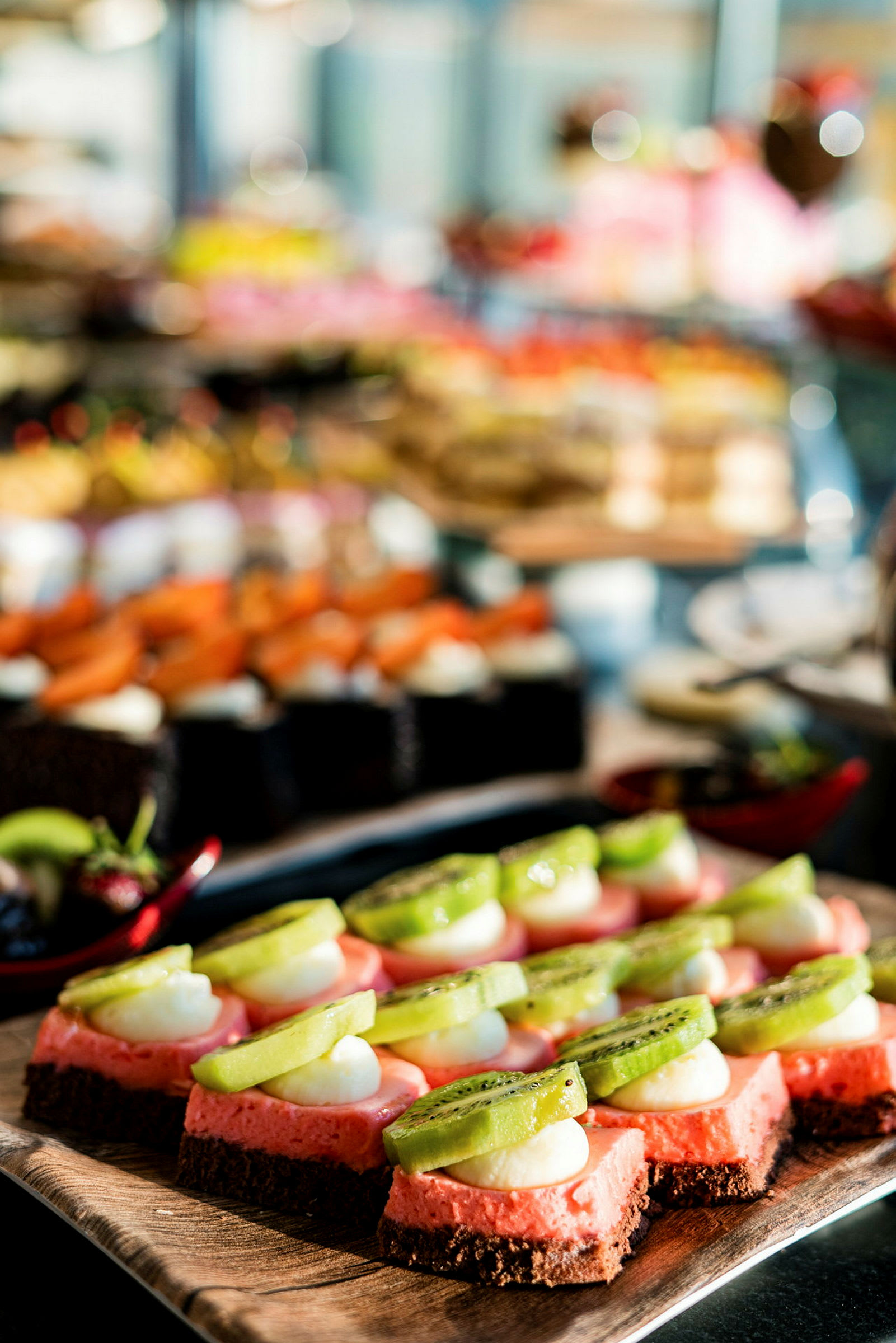 Nærbillede af små dessertstykker toppet med kiwi og fløde på en buffet. (AI-genereret tekst)