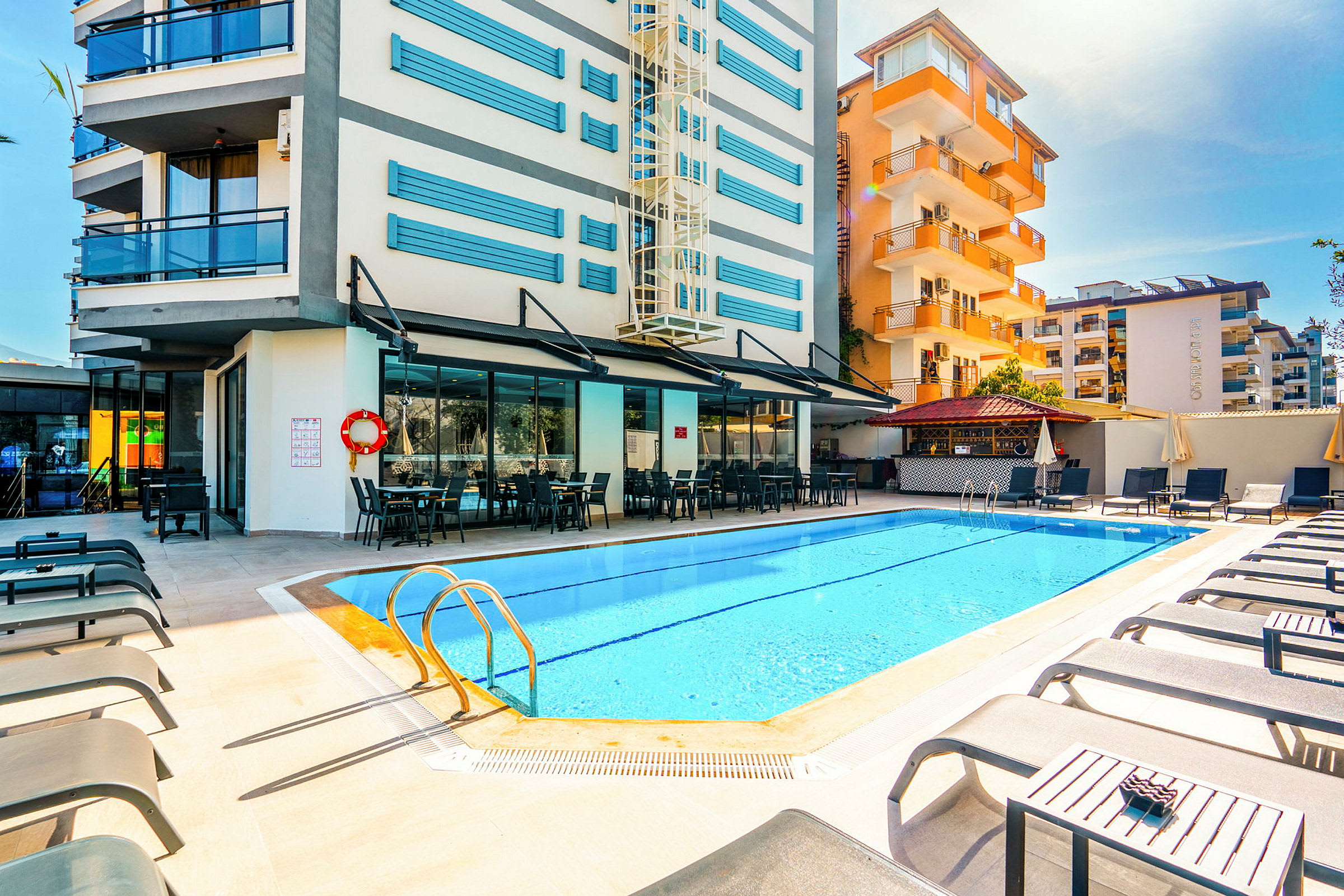 Poolområde ved hotel med liggestole og udendørs servering. (AI-genereret tekst)