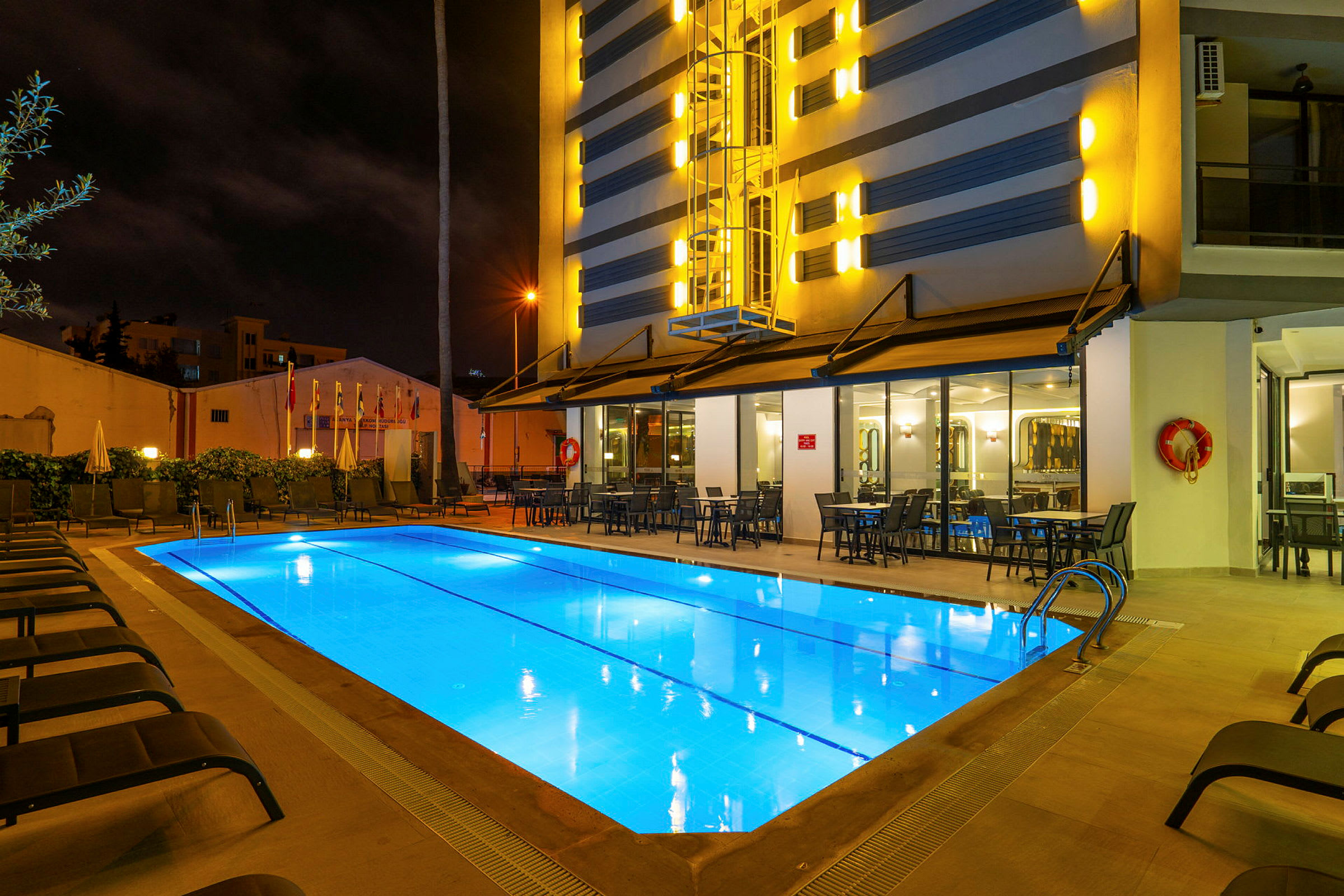 Udendørs pool ved et hotel om aftenen, omgivet af liggestole og borde. (AI-genereret tekst)