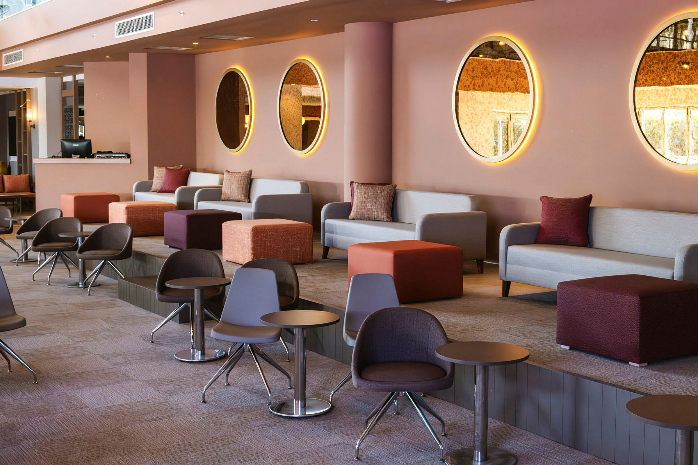 En moderne og farverig lounge med sofaer, små borde og runde spejle på væggen. (AI-genereret tekst)