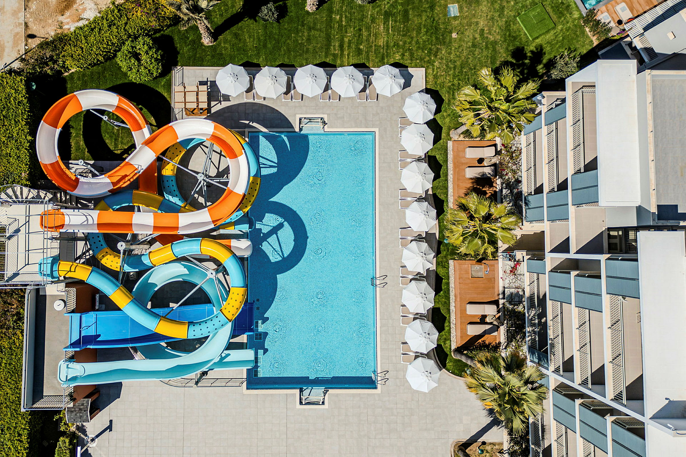 Udsigt ovenfra af en hotelpool med farverige vandrutsjebaner og liggestole. (AI-genereret tekst)