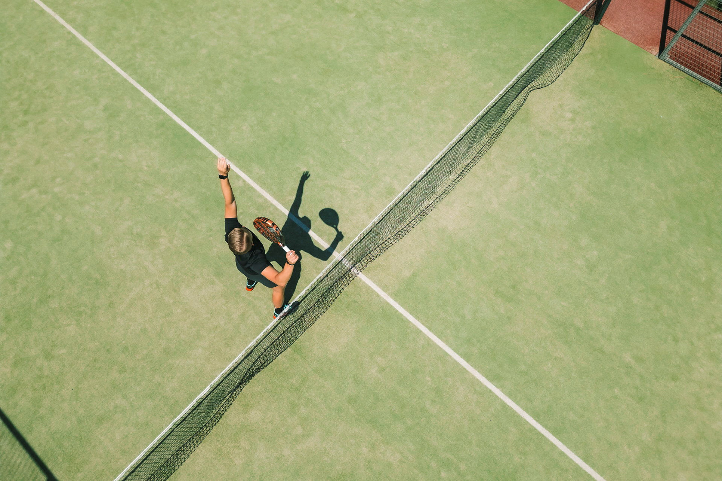 En person spiller tennis på en grøn bane og er ved at slå en bold med en ketsjer. (AI-genereret tekst)