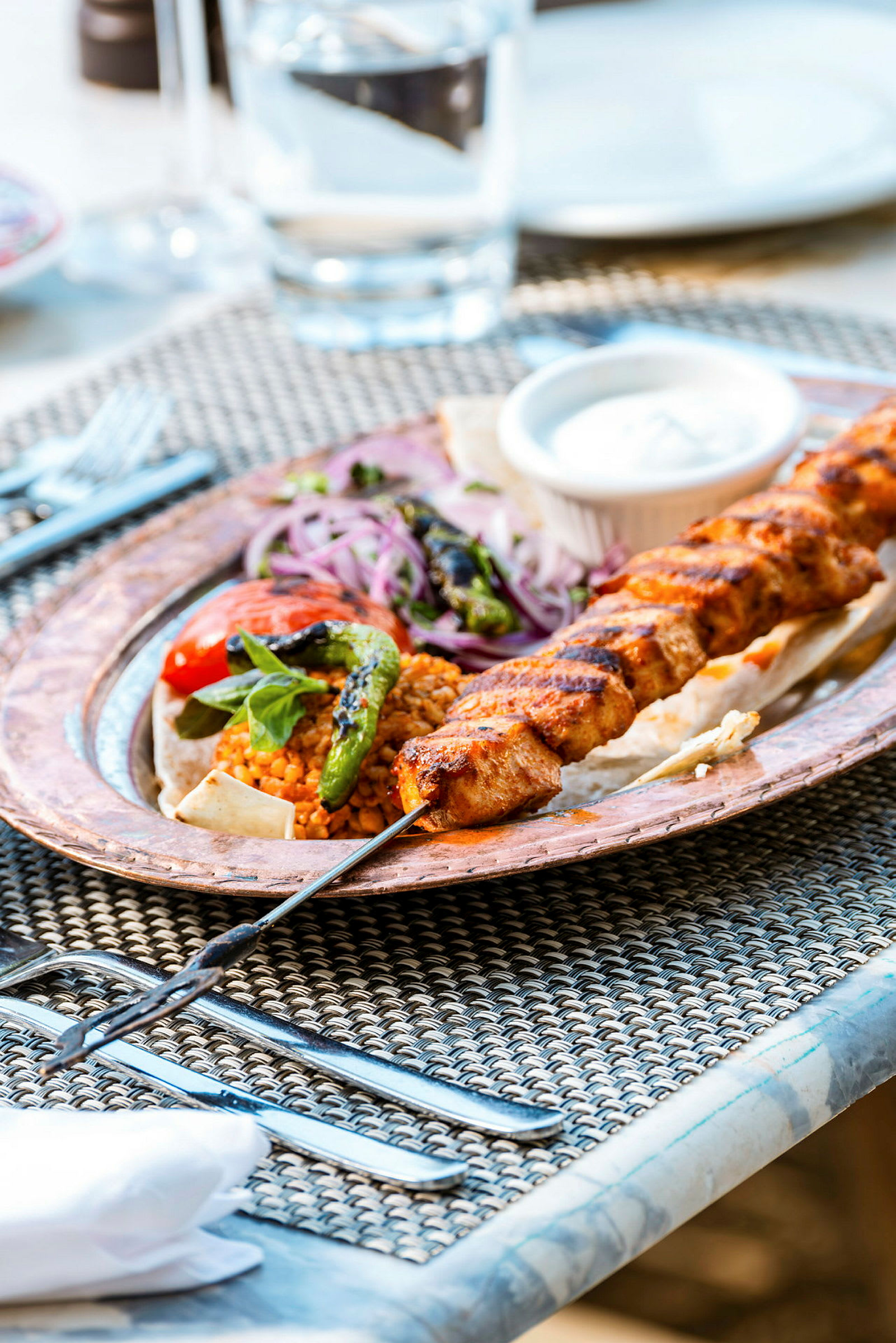 En tallerken med grillspyd, grøntsager og sauce på et bord. (AI-genereret tekst)