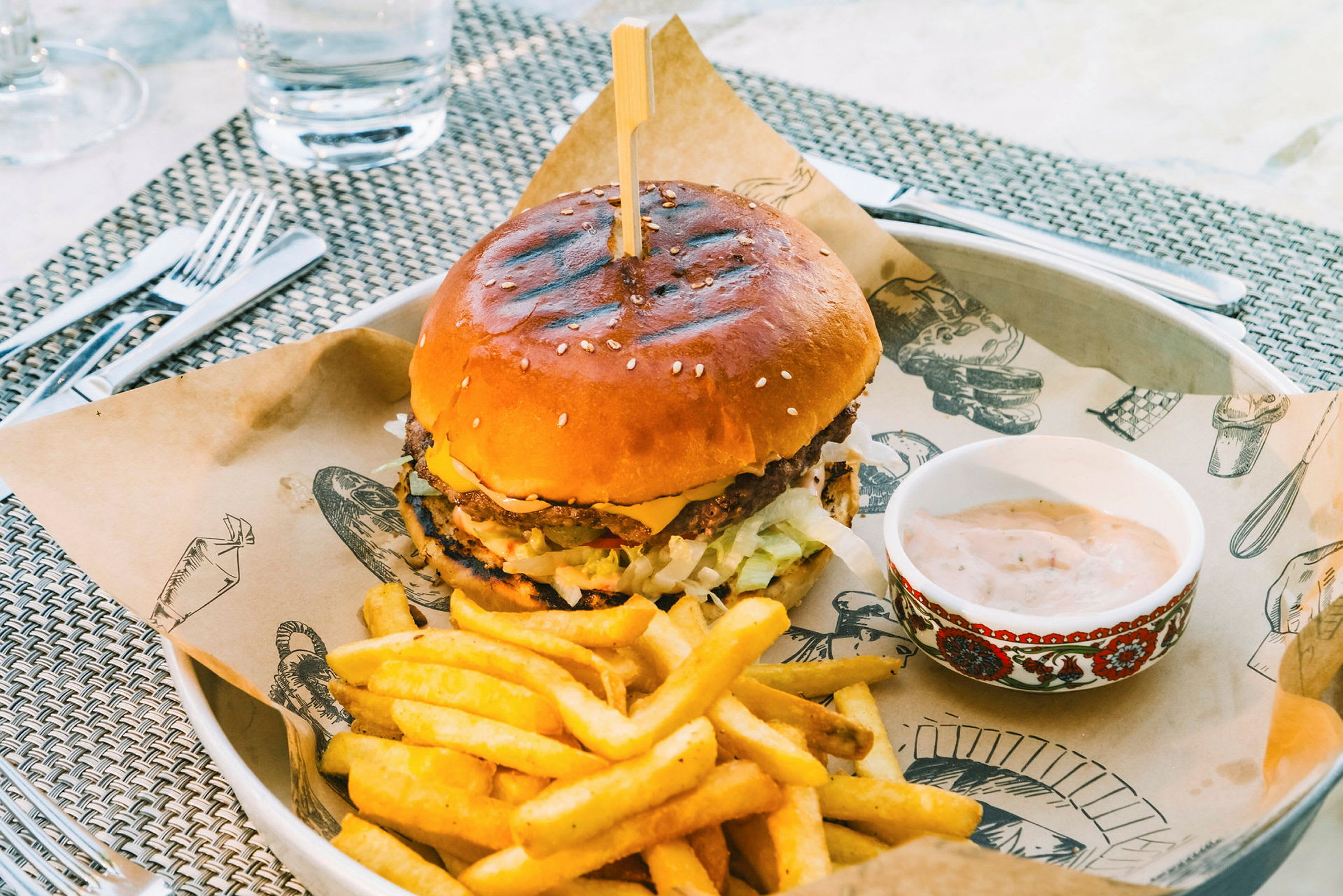 En burger serveret på en tallerken med pommes frites og en skål sovs. (AI-genereret tekst)