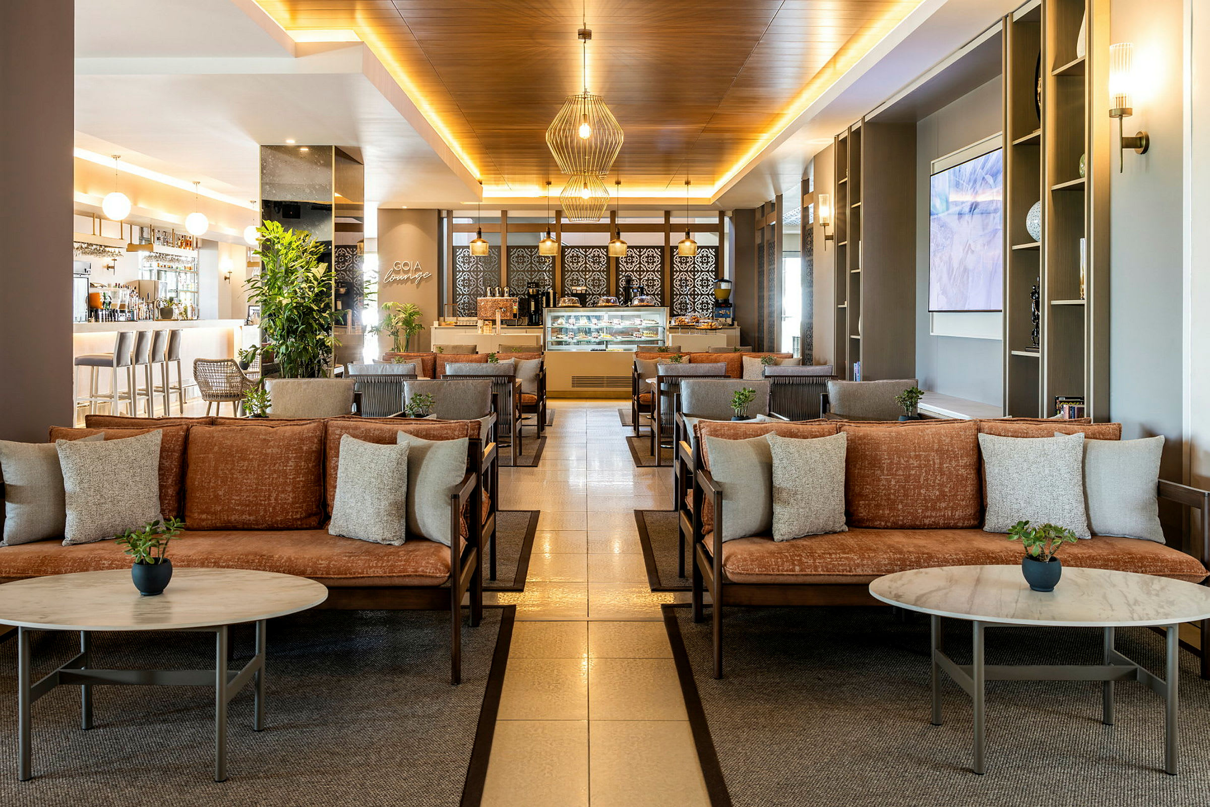 En lounge med sofaer og borde, omgivet af planter og en bar i baggrunden. (AI-genereret tekst)