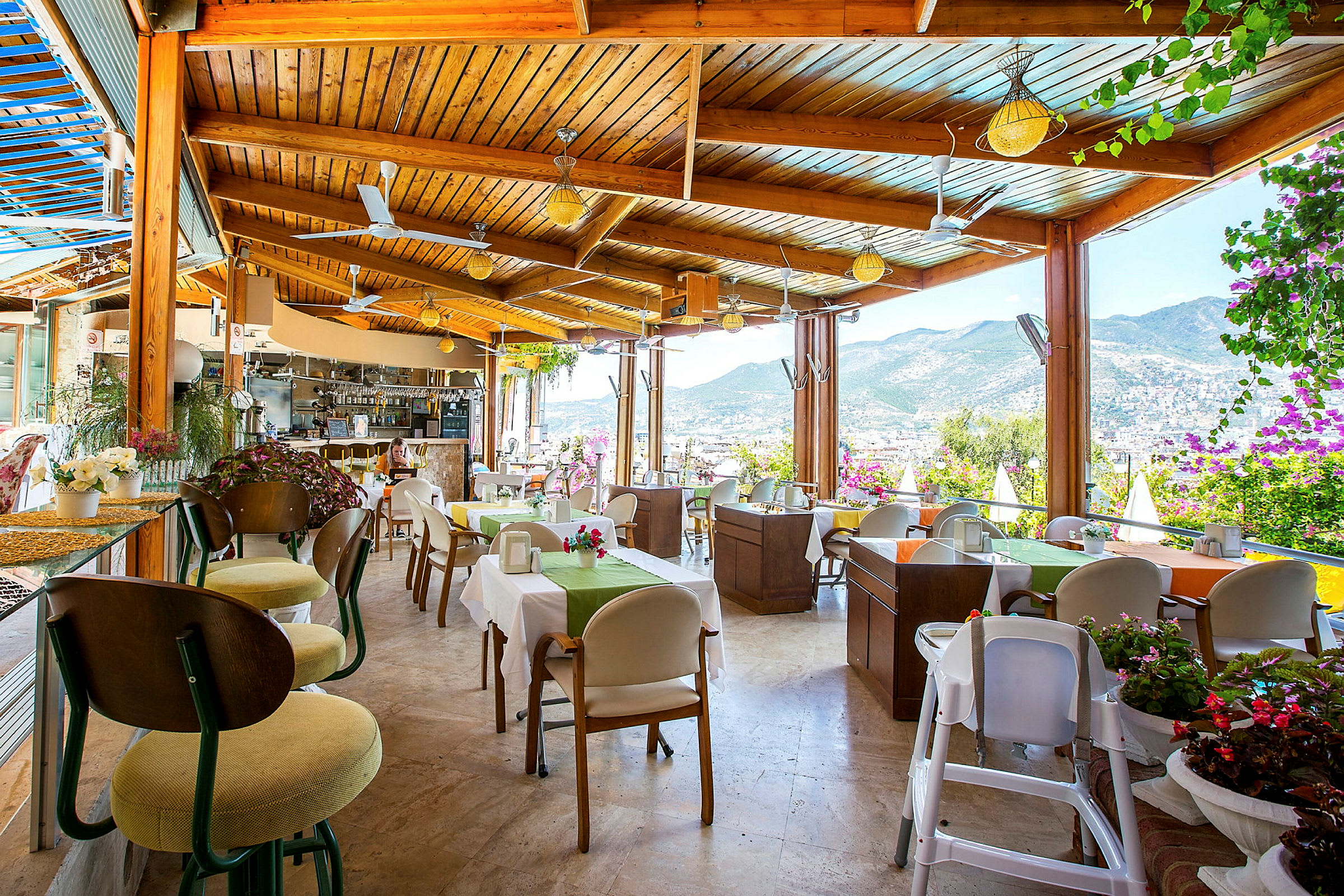 En restaurant med udsigt over bjergene og byen, med borde dekoreret med blomster. (AI-genereret tekst)
