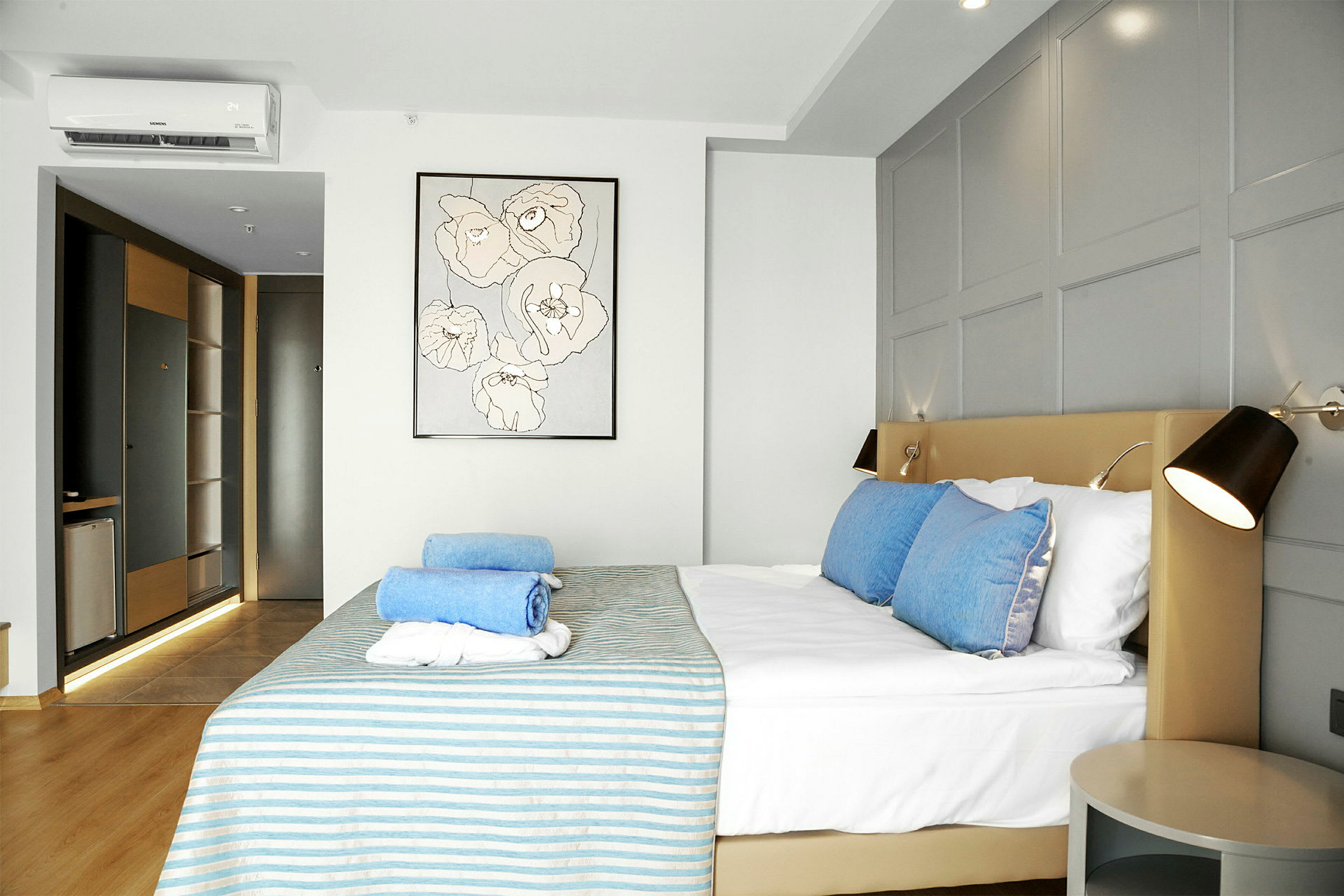 Moderne indrettet hotelværelse med en seng dekoreret med blå og hvide håndklæder, et maleri på væggen og et sidebord. (AI-genereret tekst)