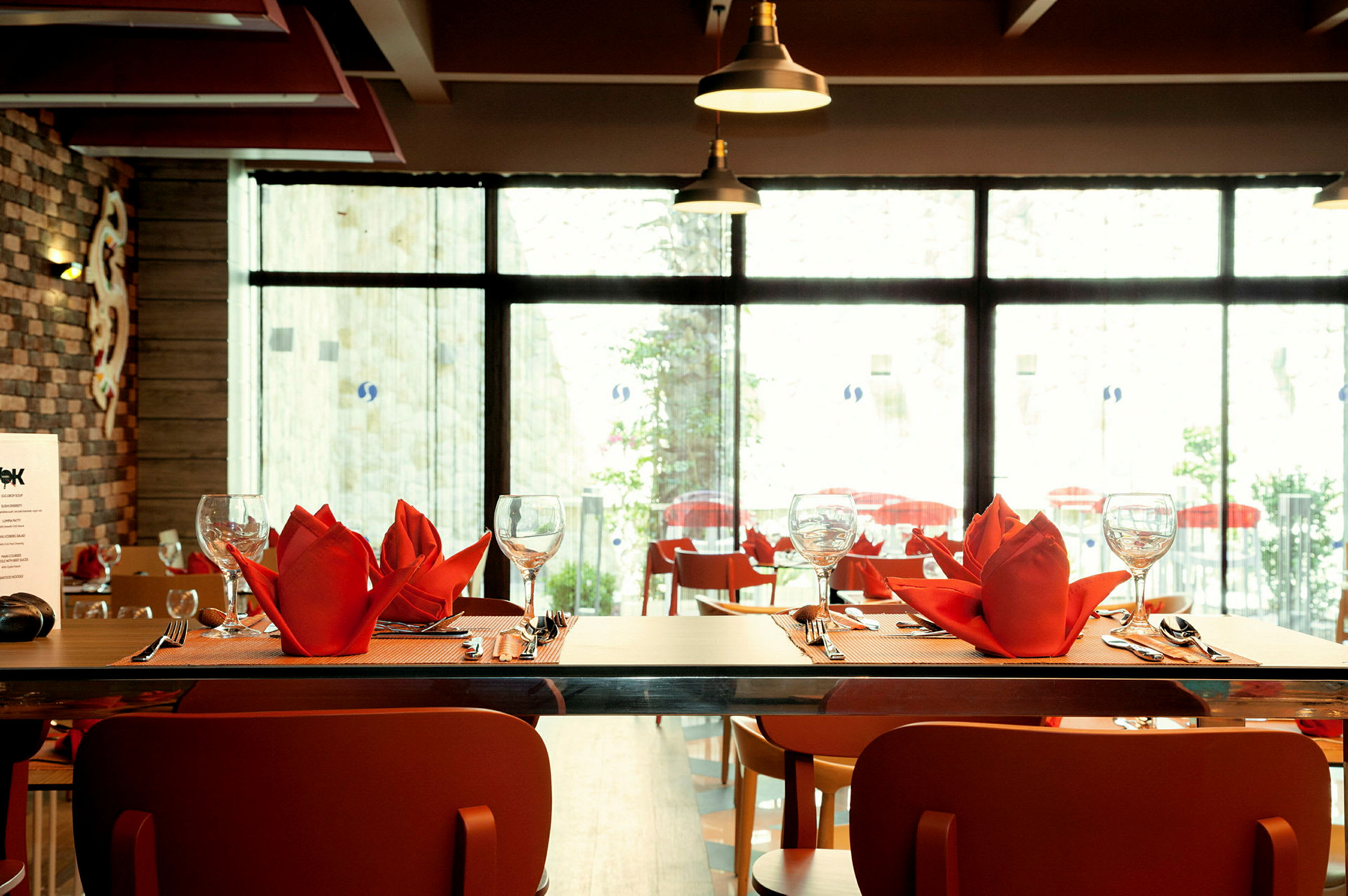 Bord på restaurant med røde servietter, glas og bestik dækket op. (AI-genereret tekst)