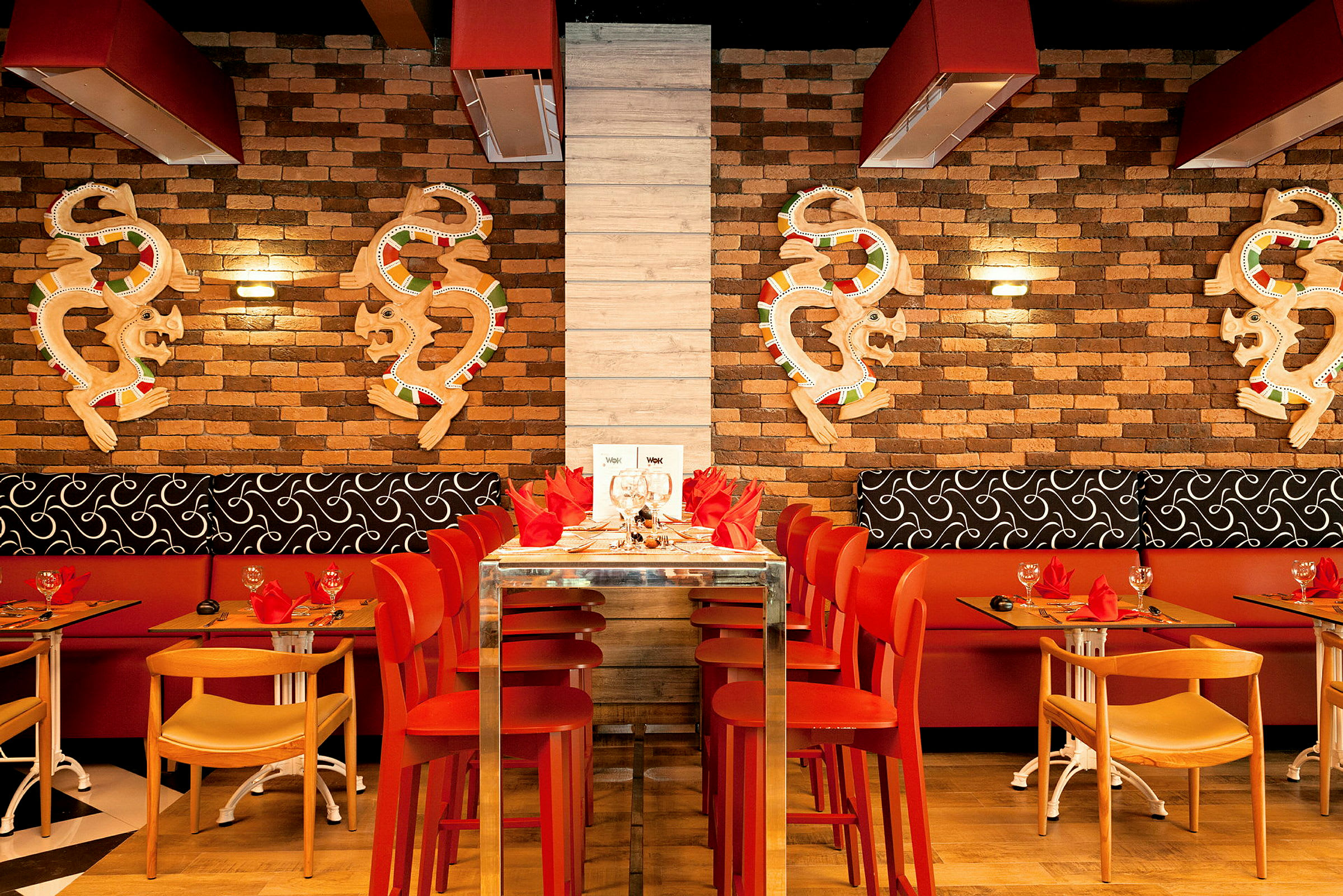 En restaurantindretning med røde stole og en murstensvæg dekoreret med kunstværker. (AI-genereret tekst)
