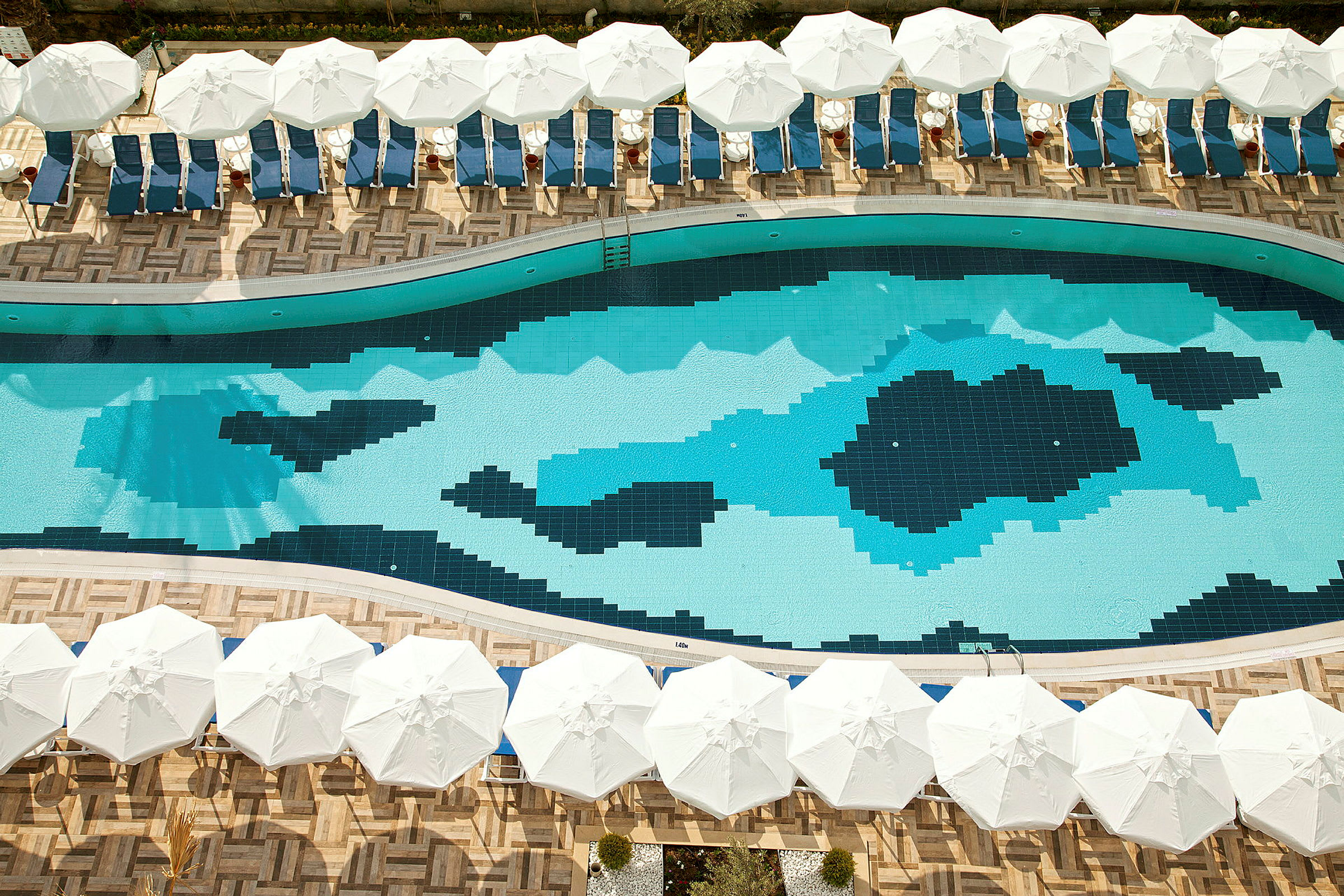 En swimmingpool med mønstrede mosaikfliser omgivet af liggestole og hvide parasoller. (AI-genereret tekst)