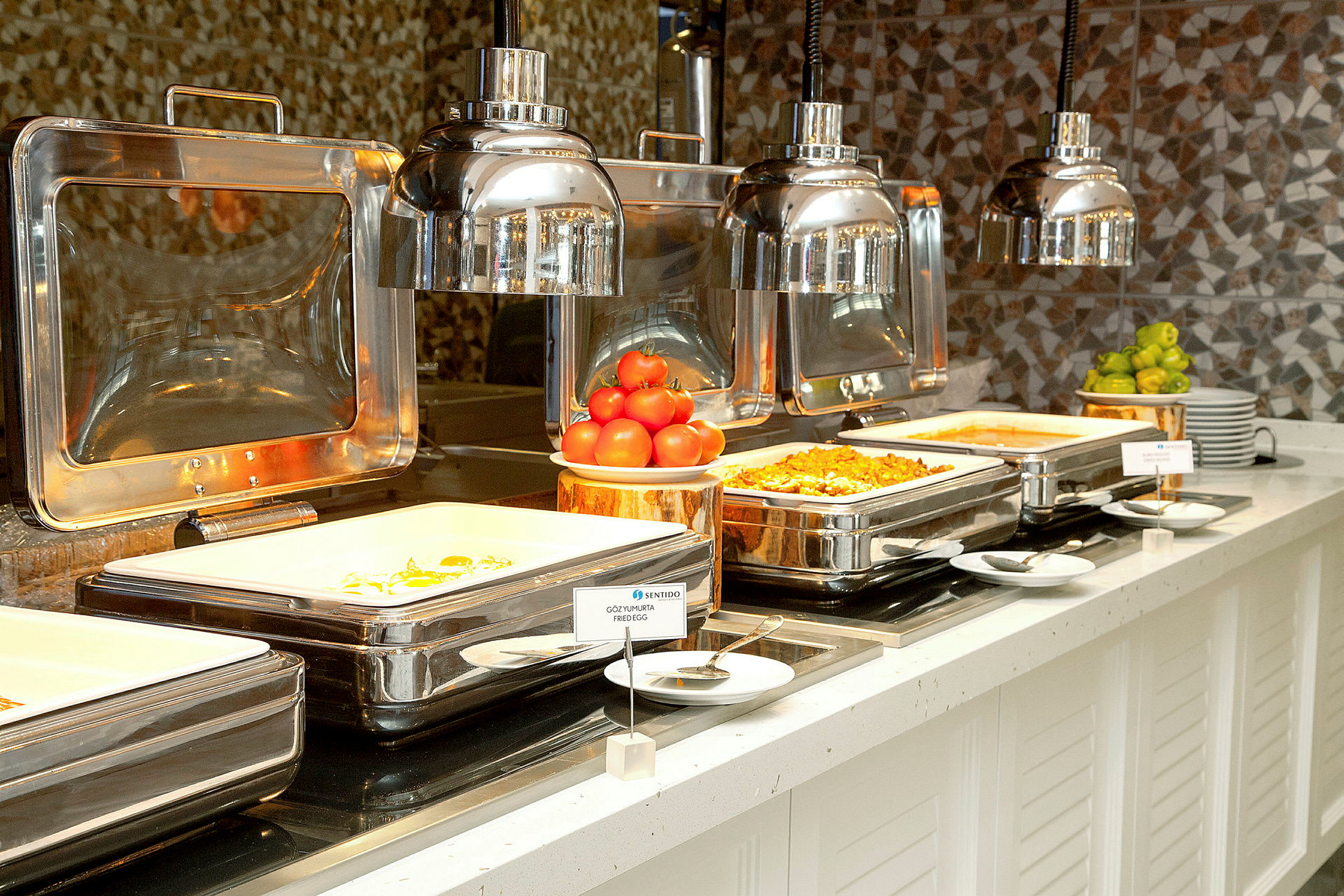Buffetbord med mad i serveringsbeholdere og dekorationer af tomater og lime. (AI-genereret tekst)