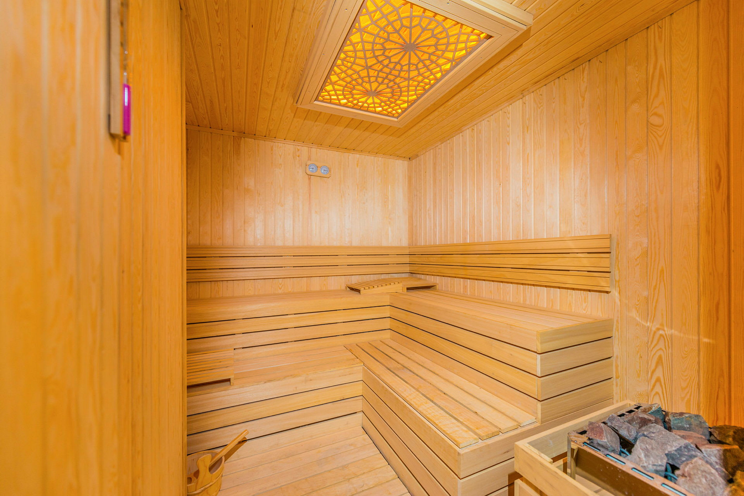 Inde i en træsauna med bænke langs væggene og en mønstret lampe i loftet. (AI-genereret tekst)