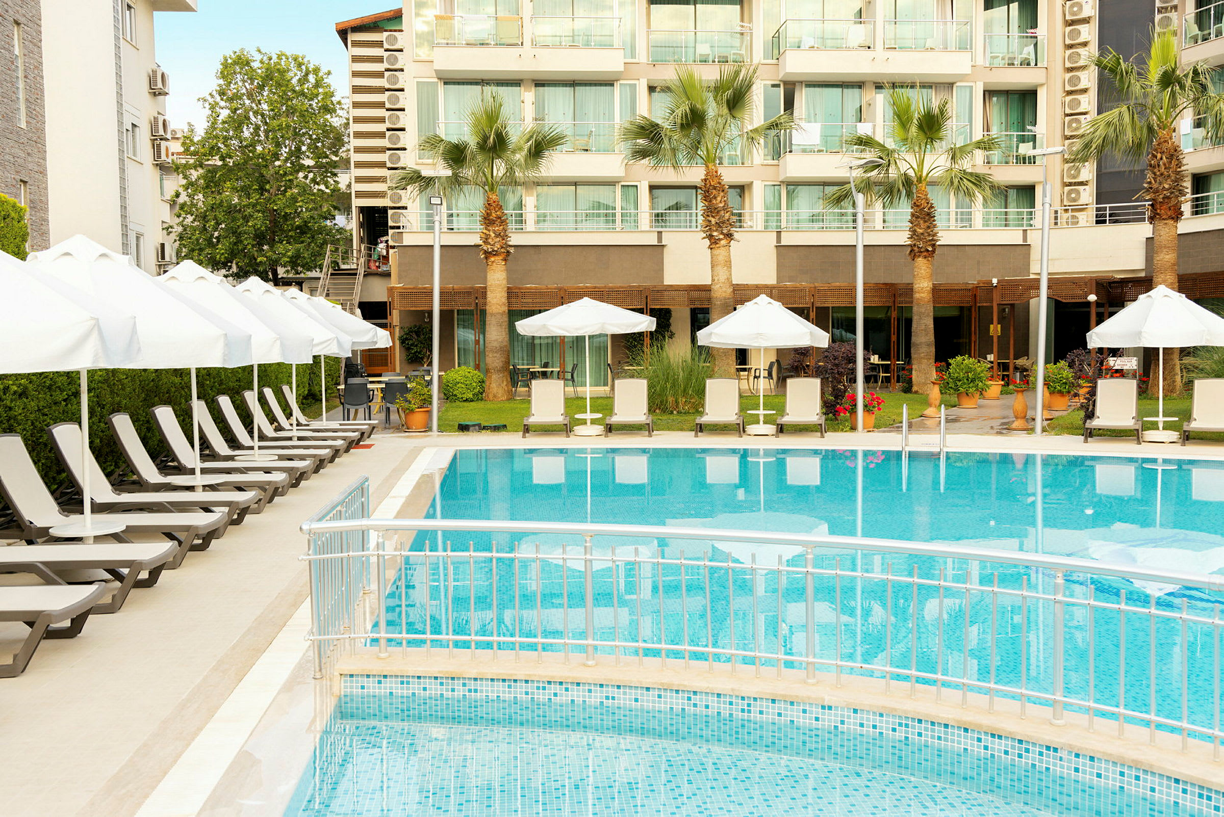 Udendørs pool med liggestole og parasoller foran et hotel. (AI-genereret tekst)