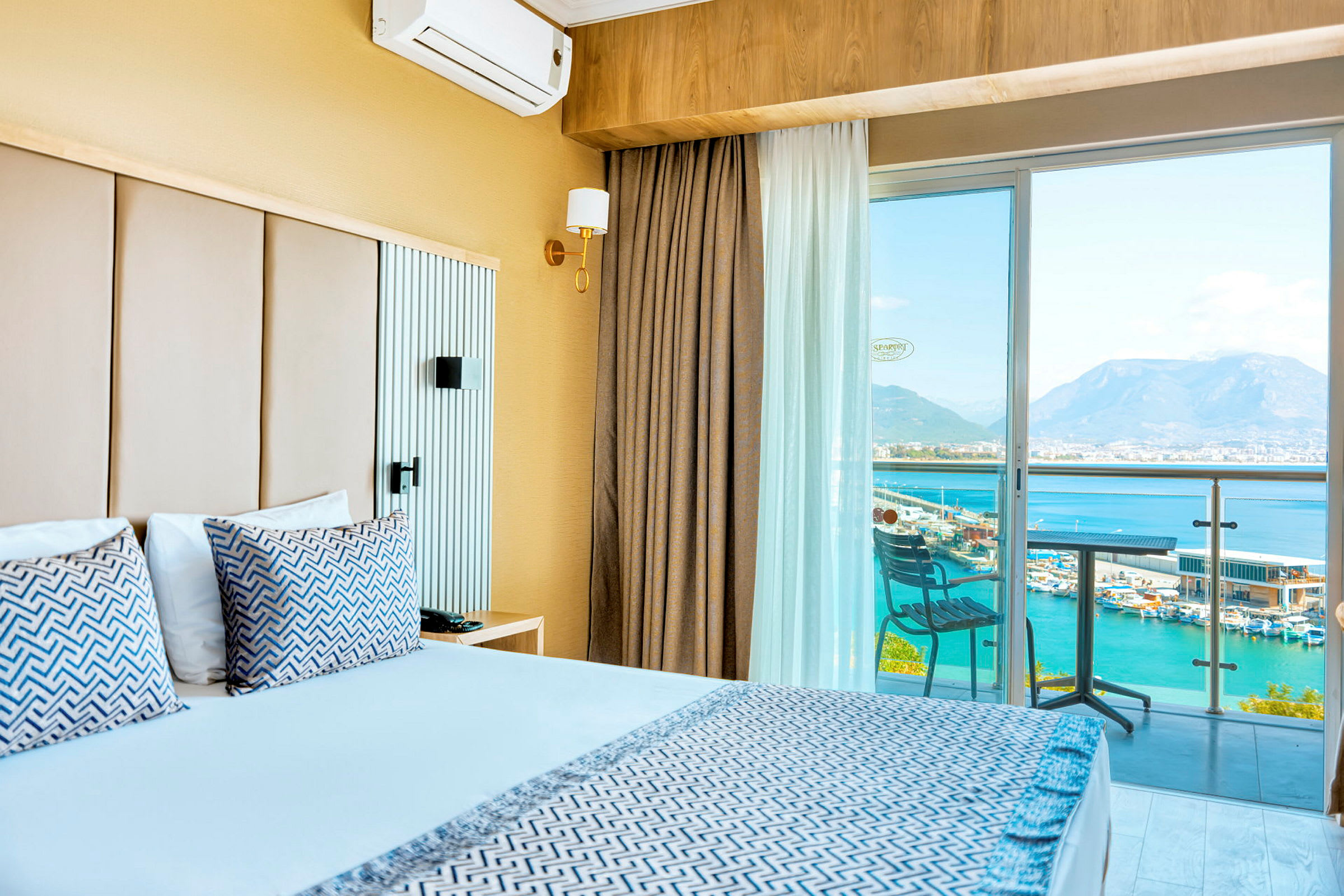 Hotelværelse med dobbeltseng, balkon med udsigt over havet og bjergene. (AI-genereret tekst)