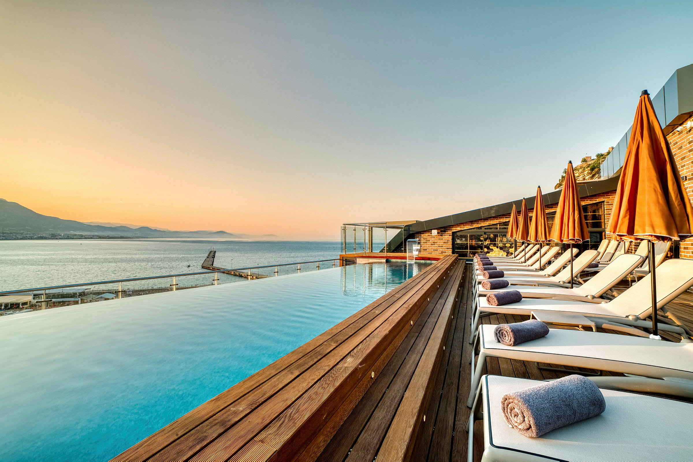 Strandområde med swimmingpool, liggestole og orange parasoller. (AI-genereret tekst)