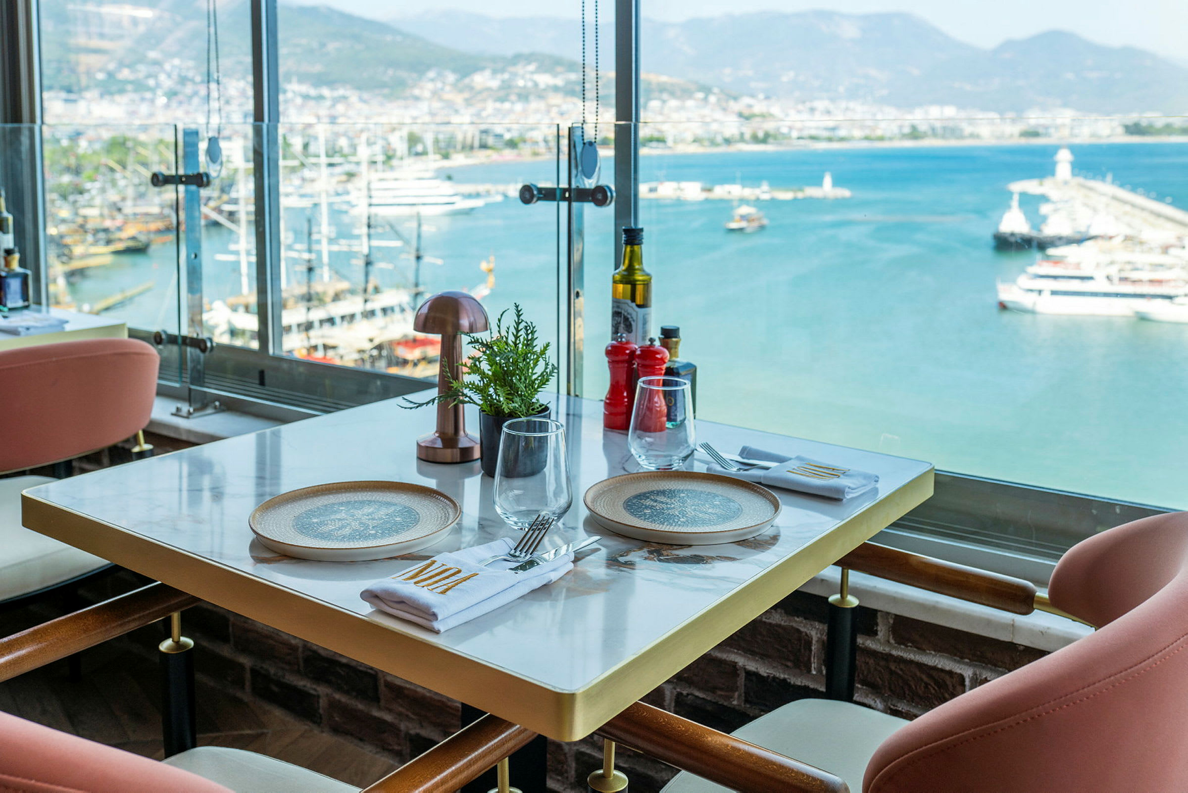 Udsigt fra en restaurantbordopdækning med en havn og havet i baggrunden. (AI-genereret tekst)