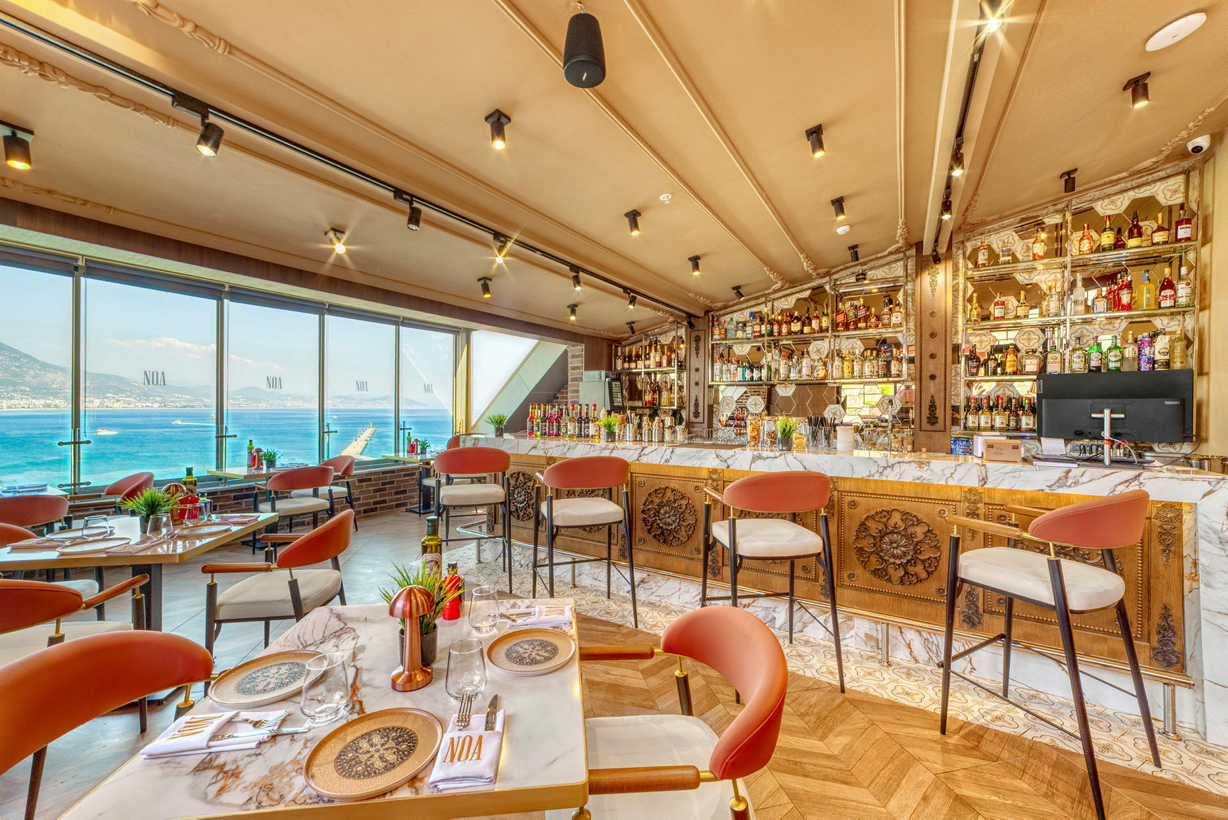 Restaurant med udsigt over havet, borde og stole, samt en veludstyret bar. (AI-genereret tekst)